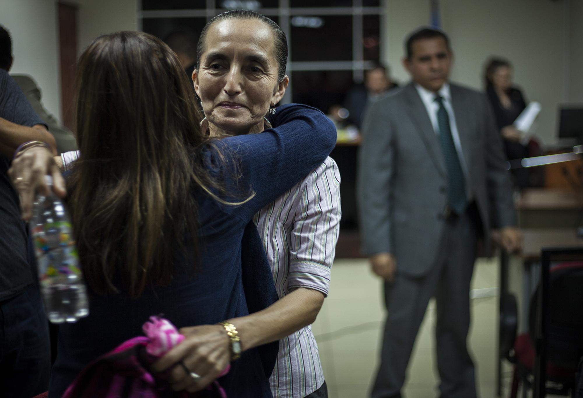 Dorila Márquez es recibida por su hija luego de brindar su testimonio en la audiencia sobre la masacre de El Mozote y lugares aledaños. Márquez declaró durante el juicio que se realiza en el juzgado de San Francisco Gotera, en el departamento de Morazán, el viernes 13 de octubre. Al fondo, el abogado defensor, Lisandro Quintanilla, quien admitió en declaraciones que, el 11 de diciembre de 1981, sí ocurrió una masacre. Foto de El Faro: por Víctor Peña.