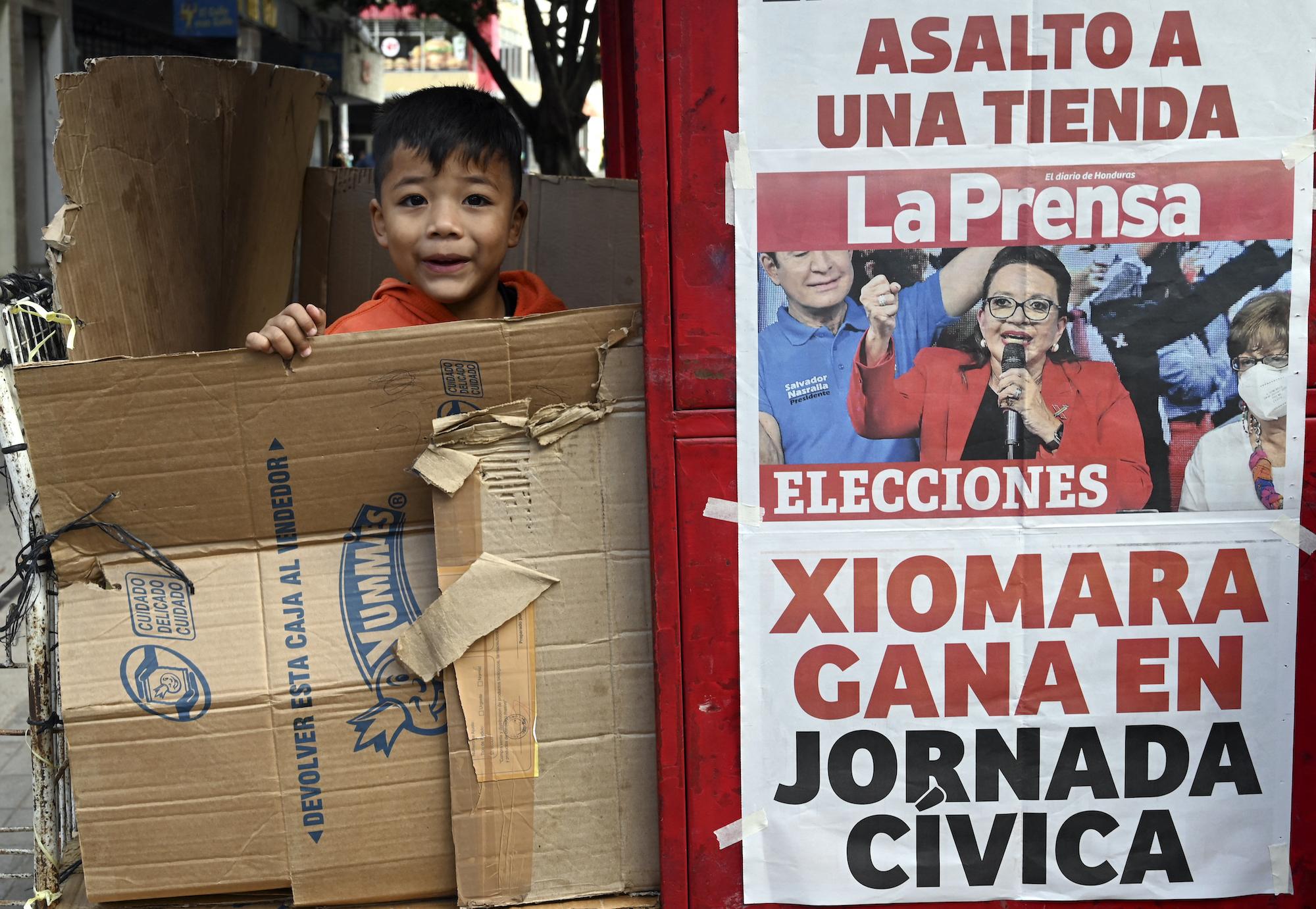 Un niño juega junto a una venta de periódicos en cuya portada se recoge la victoria de Xiomara Castro en las elecciones del pasado 28 de noviembre 2021. Foto: Orlando Sierra / AFP.