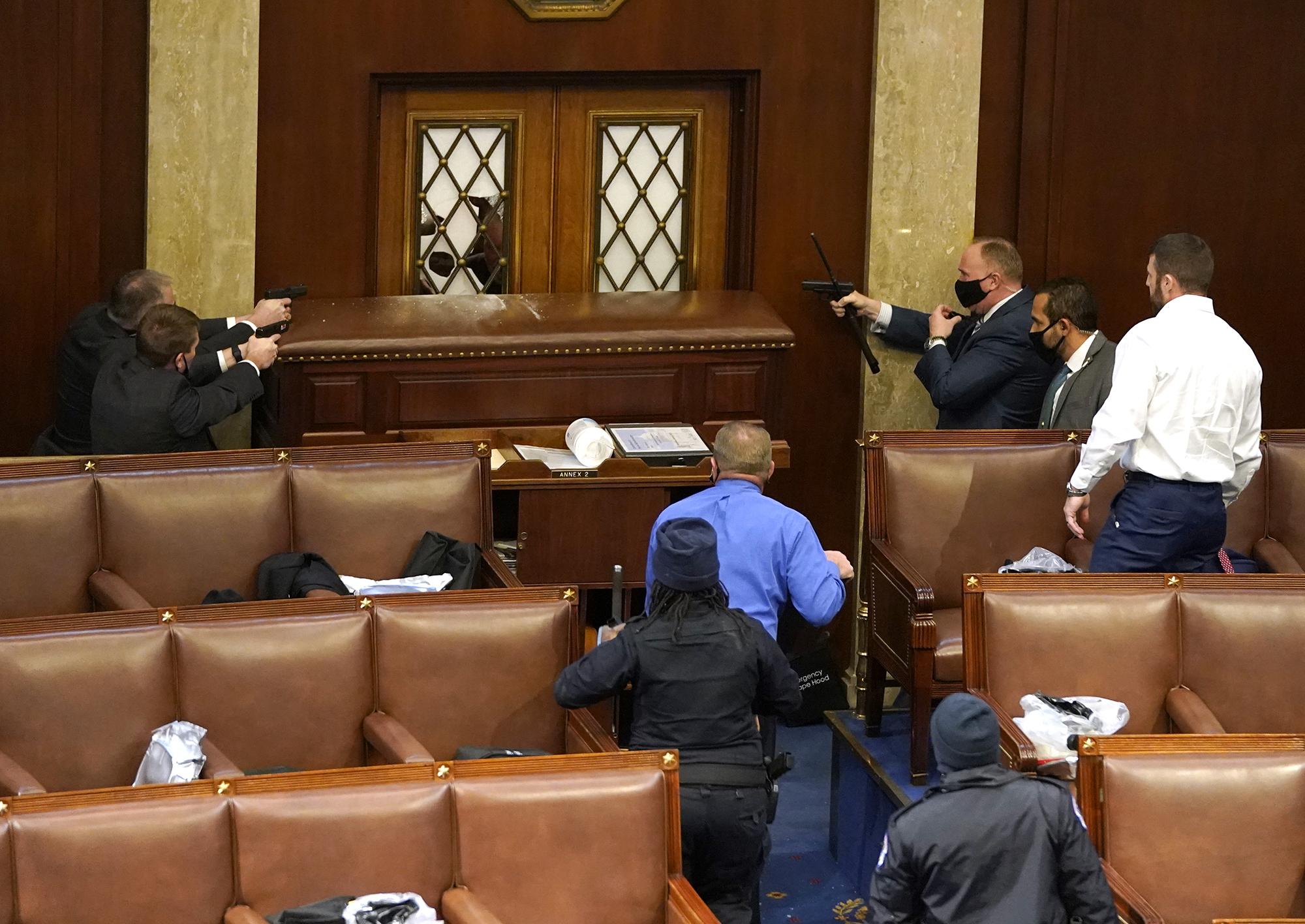 Oficiales de policía del Capitolio de los Estados Unidos apuntan con sus armas a una puerta que fue vandalizada en la Cámara durante una sesión conjunta del Congreso, que celebró una sesión conjunta hoy para ratificar la victoria del Colegio Electoral 306-232 del presidente electo Joe Biden sobre el presidente Donald Trump. Un grupo de senadores republicanos dijo que rechazarían los votos del Colegio Electoral de varios estados a menos que el Congreso nombrara una comisión para auditar los resultados de las elecciones. Foto de El Faro: Drew Angerer / Getty Images / AFP.