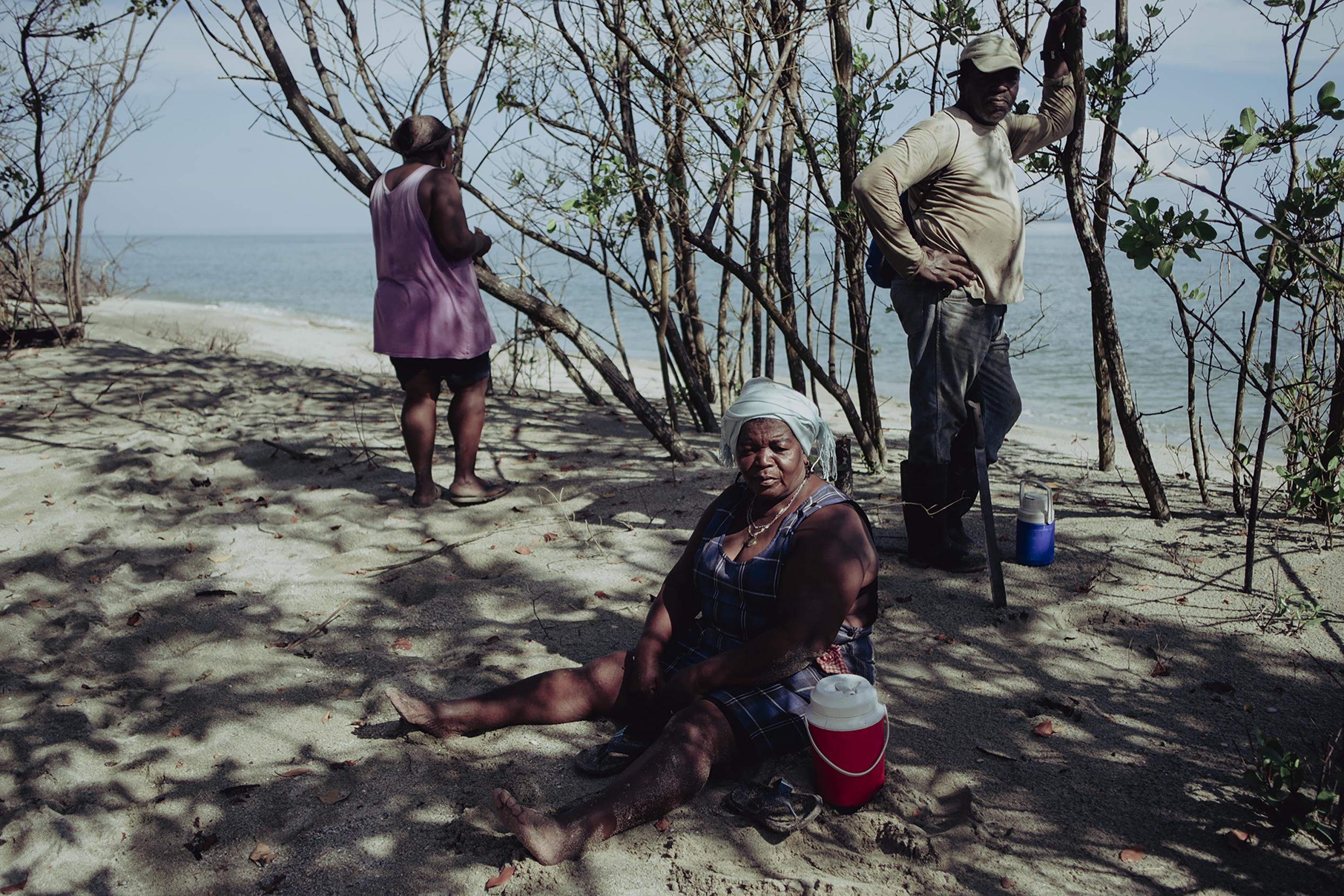 Justa Robledo, al centro, María Robledo y Víctor Sacasa toman un descanso en la playa de África, Nueva Armenia, durante una mañana de trabajo comunal de recolección de madera para la construcción de Casas Ancestrales de la Salud. Para los garífunas el trabajo comunal es importante, en Nueva Armenia por ejemplo la unidad comunal le ha servido para recuperar los territorios de los que en los 90 habían sido despojados, 