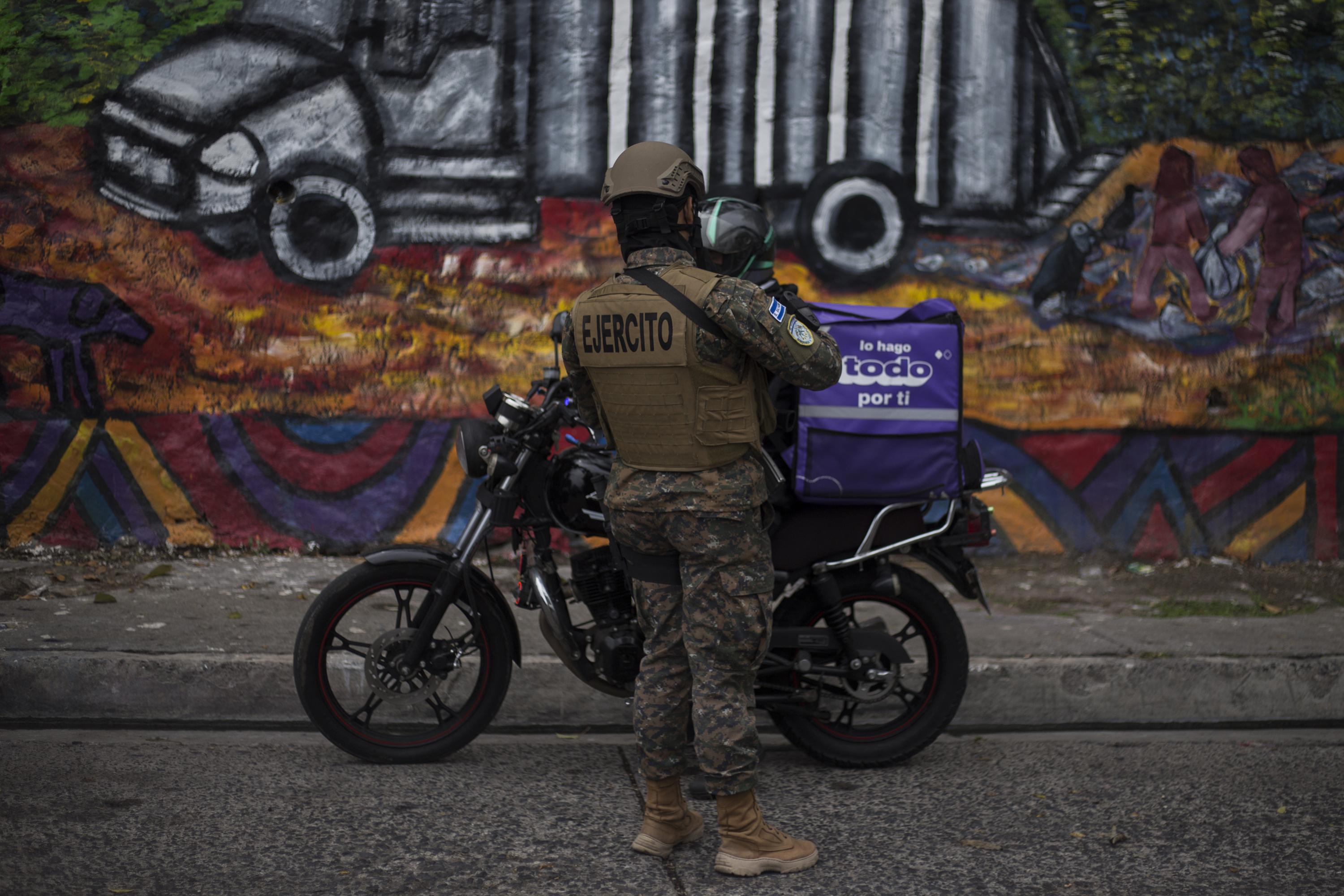 Un militar registra a un repartidor de comida sobre la calle principal de la comunidad 22 de Abril, en el municipio de Soyapango.  Este tipo de registros son cotidianos en el marco del Régimen de Excepción. Se hacen principalmente en comunidades de San Salvador con alta presencia pandillera. Foto de El Faro: Víctor Peña. 