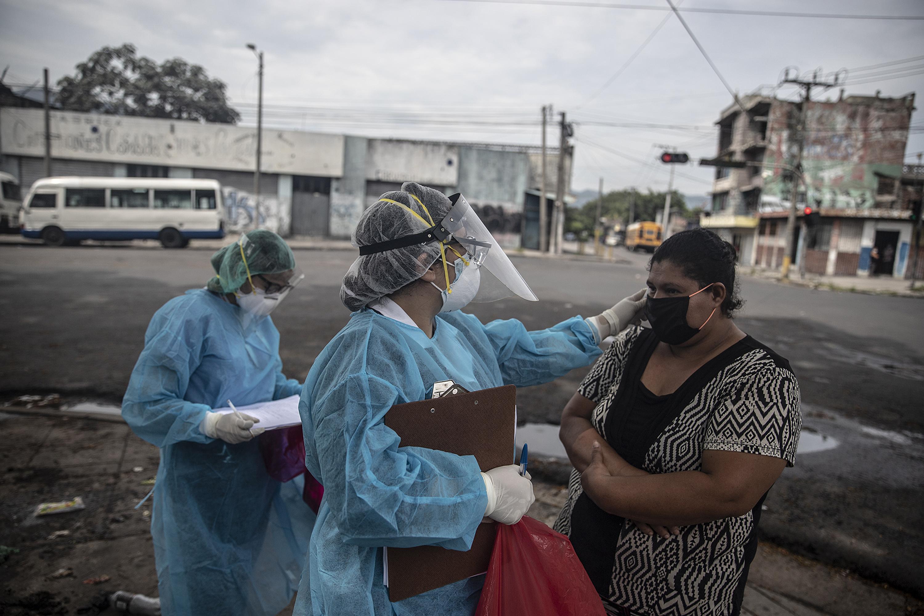 Dos trabajadoras del Ministerio de Salud toman la temperatura a María del Carmen Montoya en la avenida Independencia de San Salvador. Cuatro días antes de la escena, el esposo de María fue hospitalizado por síntomas relacionados con la covid-19 en mayo del 2020. Foto de El Faro: Carlos Barrera.