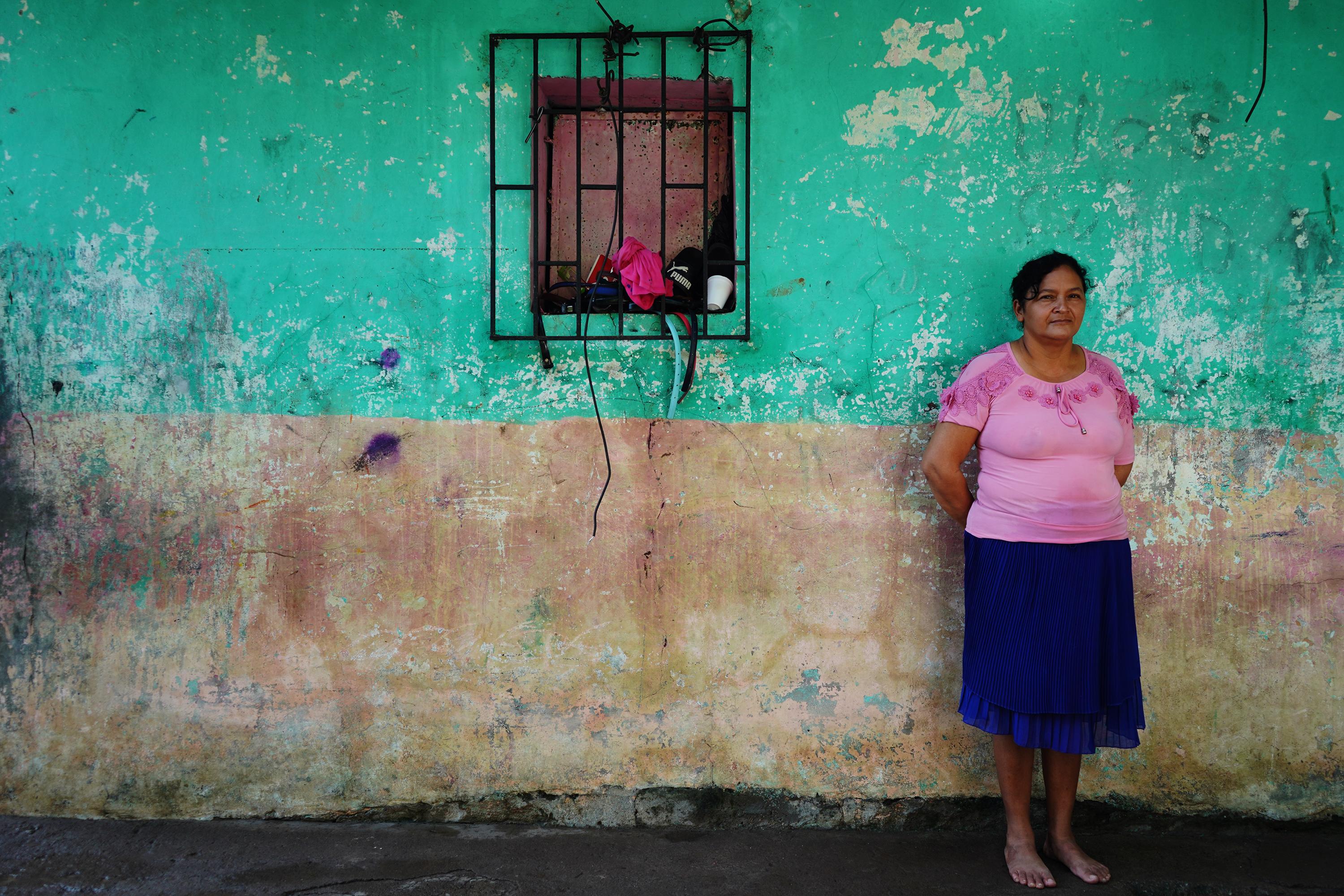 Benilda Álvarez Garay, de 48 años, vive de la venta ambulante de mascarillas, papel mata moscas, manteles y gabachas en los mercados de San Miguel. Benilda vive en la comunidad El Tiangue, en la ribera del río Grande, y una parte de su casa fue destruida durante la tormenta Julia. Su hija perdió su casa por completo. “Al oír cómo tronaba el río, yo pensé que un derrame me iba a dar de tanto llorar y de tanta preocupación. Ya son dos veces que esto me pasa. También me pasó con el Mitch”, dice Benilda mientras posa frente a las grietas y la marca del agua en lo que quedó de su vivienda.