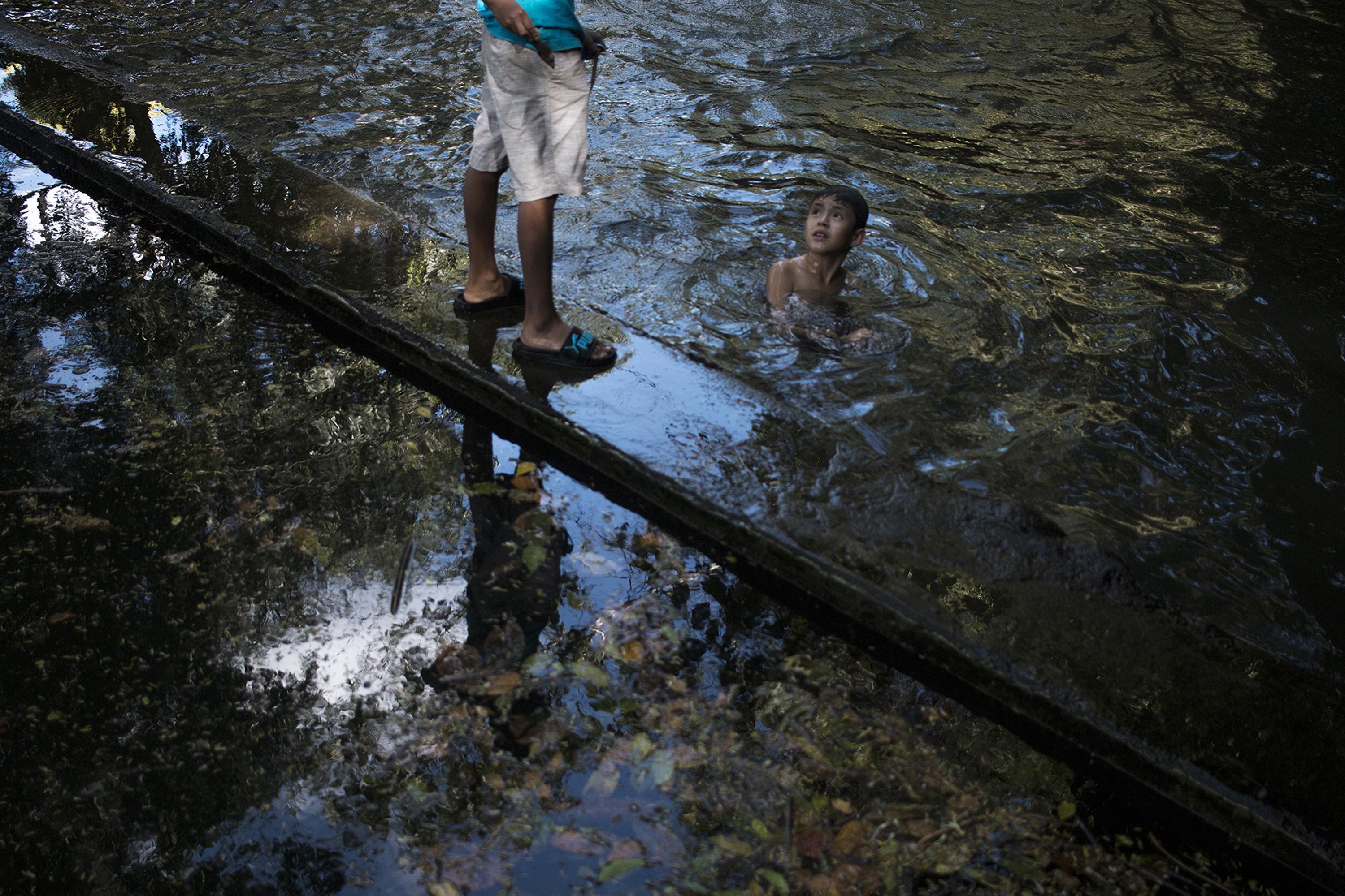 Dos menores juegan en el estanque de la Hacienda La Labor, una comunidad del departamento de Ahuachapán que desde principios de año a estado a punto de perder su único privilegio: el agua que abastece a más de 500 familias. Fénix, una empresa inmobiliaria, realiza la construcción de 1,764, un proyecto que amenaza con quitar el agua a la comunidad. El estanque principal alcanza hasta para la diversión de muchas familias que cada tarde abarrotan esta piscina de 60 metros de largo. La distribución de esta agua está controlada por la comunidad, así como el mantenimiento de las instalaciones y las tuberías. Foto de El Faro: Víctor Peña. 