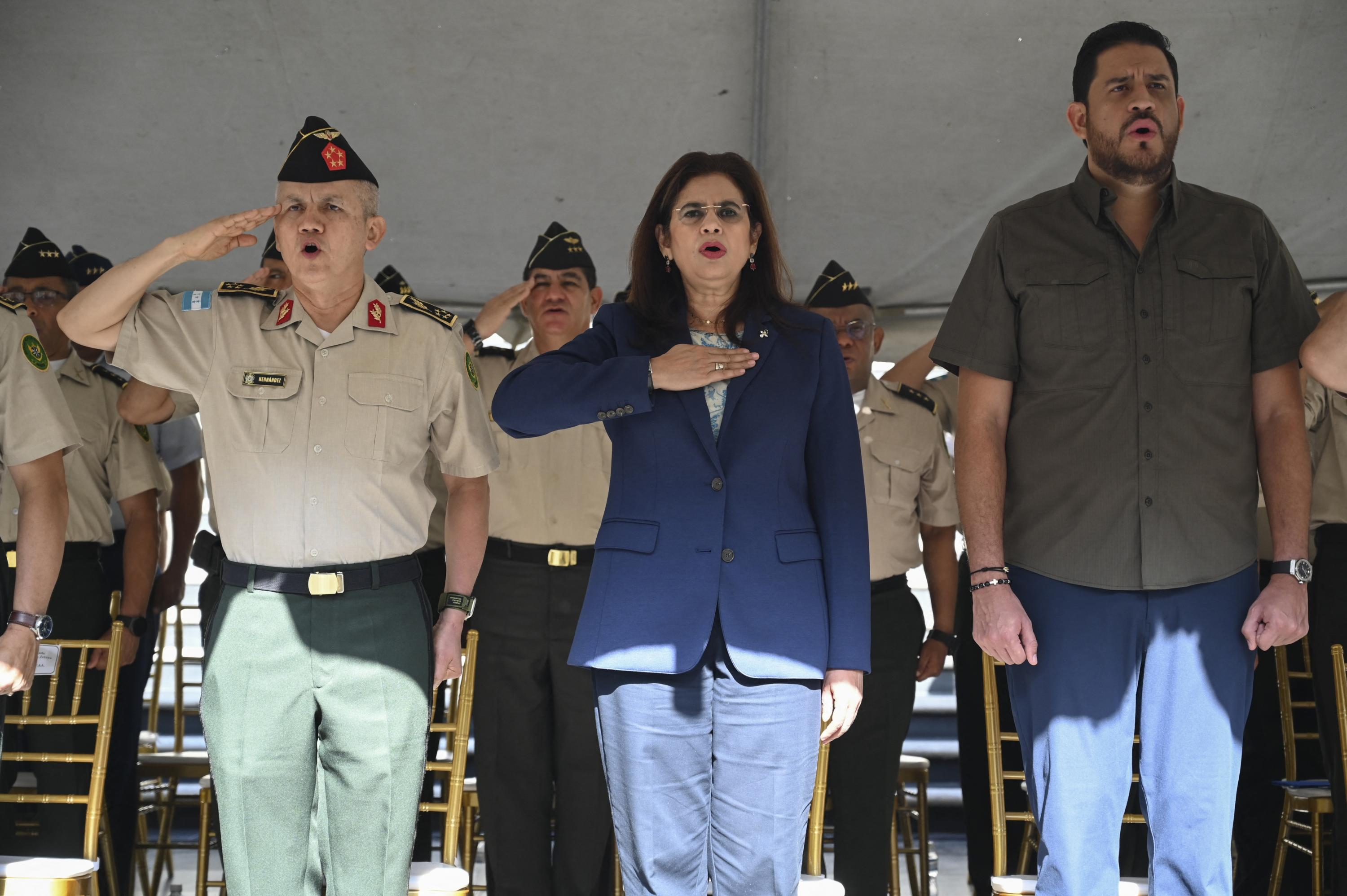 De izquierda a derecha: el jefe del Estado Mayor Conjunto de Honduras, el general Roosevelt Leonel Hernández; la nueva ministra de Defensa Rixi Moncada; y su predecesor José Manuel Zelaya saludan durante el himno nacional en la ceremonia de inauguración de Moncada en las instalaciones del Estado Mayor Conjunto. Tegucigalpa, 2 de septiembre, 2024. Foto de El Faro: Orlando Sierra/AFP