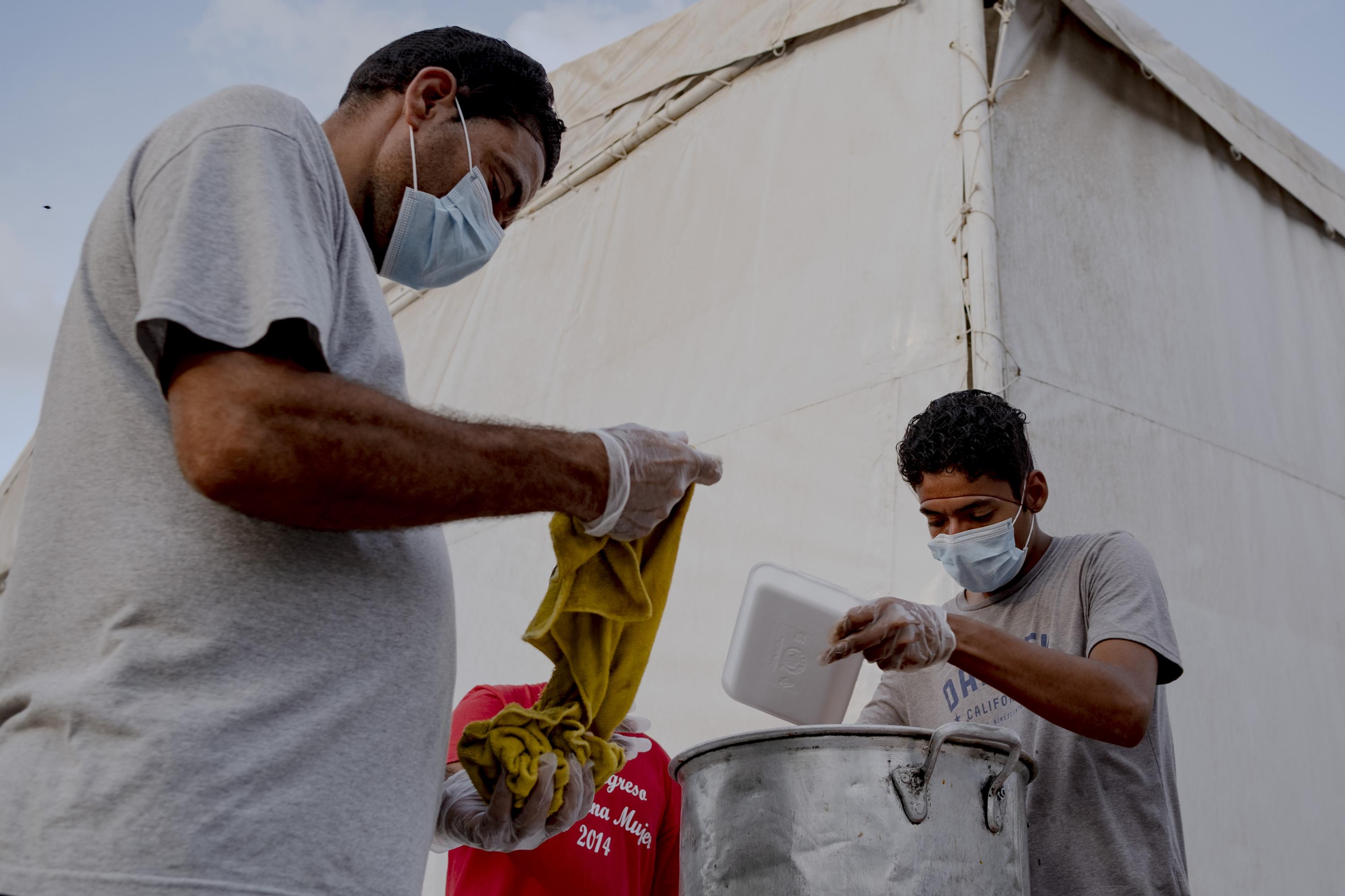 En el campamento no está establecido quiénes se encargan de servir la cena al resto de sus compañeros. Se organizan como pueden aunque ya hay referentes por zona. Desde hace un año, la comida llega a sus platos porque diferentes organizaciones civiles de Brownsville, Texas, preparaban y distrinuian los alimentos. Debido al cierre de la frontera de Estados Unidos, las mismas organizaciones pagan a un comedor local para que prepare un desayuno y una cena para cada habitante de este campamento. En la imagen, dos migrantes reparten la cena.