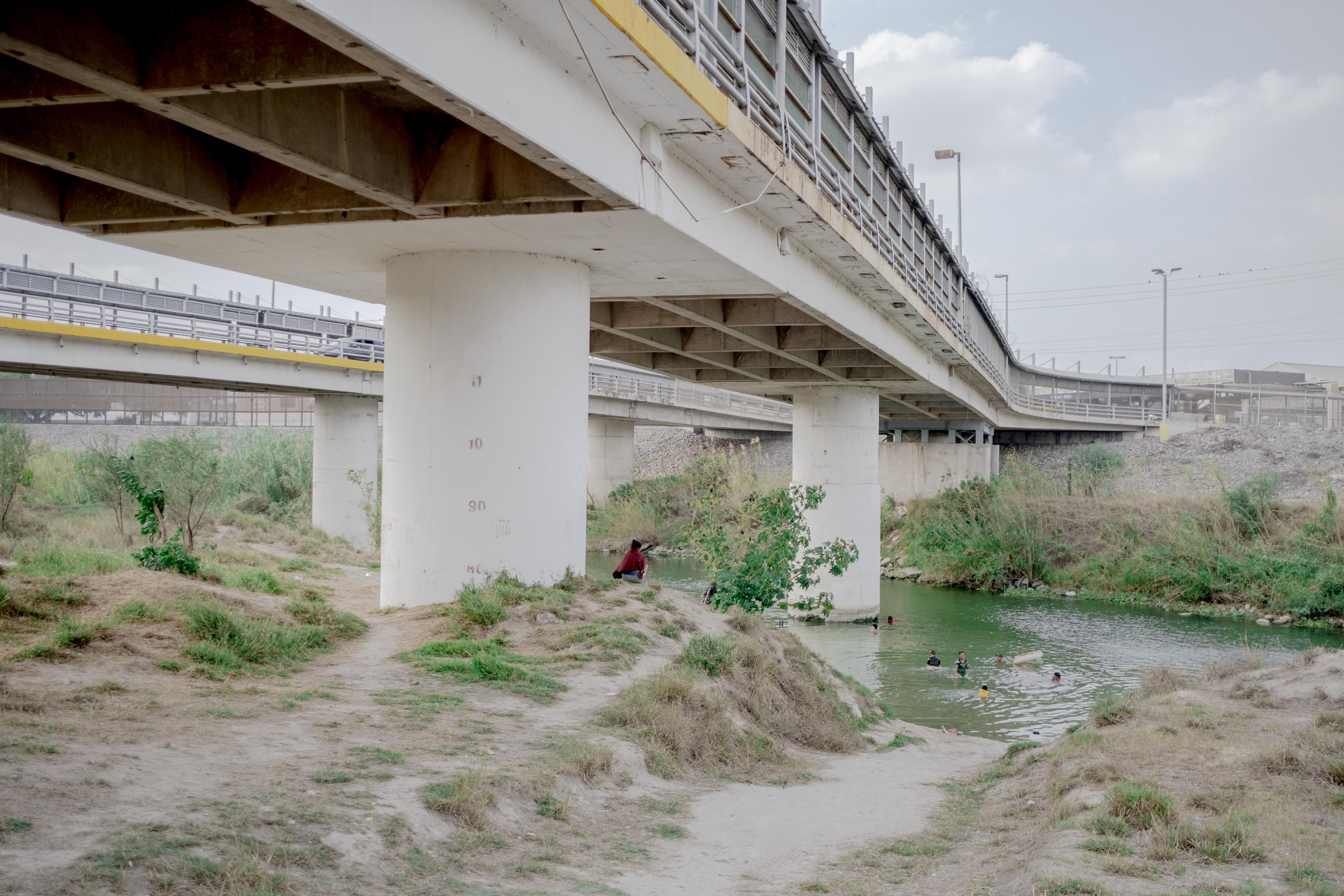 Un grupo de migrantes se baña en el río Bravo. Arriba de ellos está el puente internacional que conecta con Estados Unidos, donde transitan las personas que tienen autorización legal de entrada y de salida. Por el río Bravo aún lo intentan algunos de forma indocumentados. Esta zona es una de las más vigiladas por la Patrulla Fronteriza. 