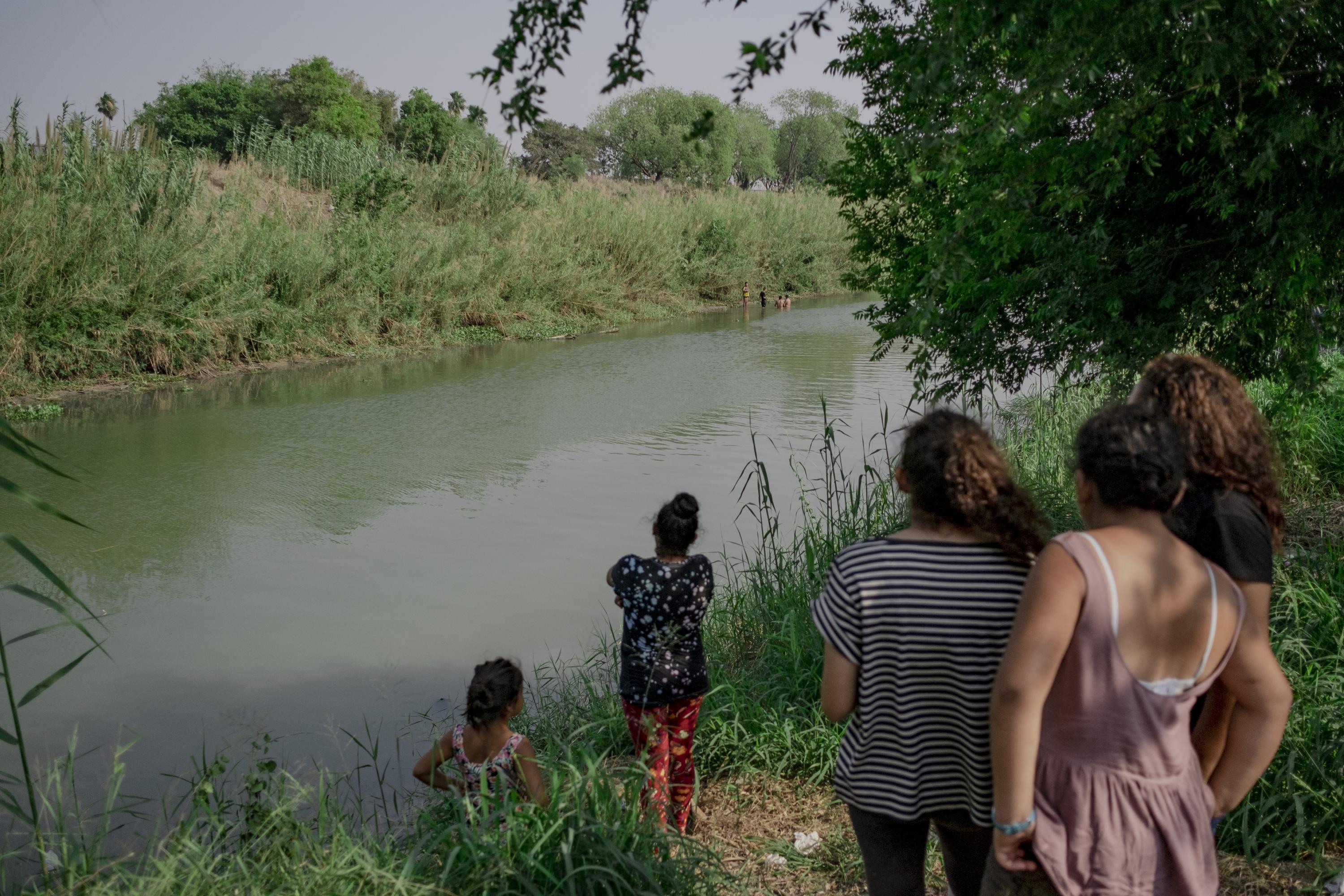 Un grupo de mujeres varadas en el campamento observa a tres migrantes que intentaron cruzar a Estados Unidos a través del río Bravo. Ellos nadaron hacia el otro lado del río. No lo lograron porque varias patrullas fronterizas los detectaron. Los tres migrantes decidieron volver al lado mexicano. Según fuentes del campamento, en algunos casos estos intentos de cruce tienen como objetivo distraer a las autoridades estadounidenses mientras grupos criminales trasladan ilícitos por otros puntos de la frontera. Esta fotografía fue tomada de forma discreta, pues La Maña, como se conoce al Cártel del Golfo en la zona, vigilaba el cruce desde una camioneta. A 500 metros de este lugar está una cruz conmemorativa en el punto del río en el que murieron Óscar y Valeria, los salvadoreños cuya fotografía dio vuelta al mundo cuando murieron ahogados. 