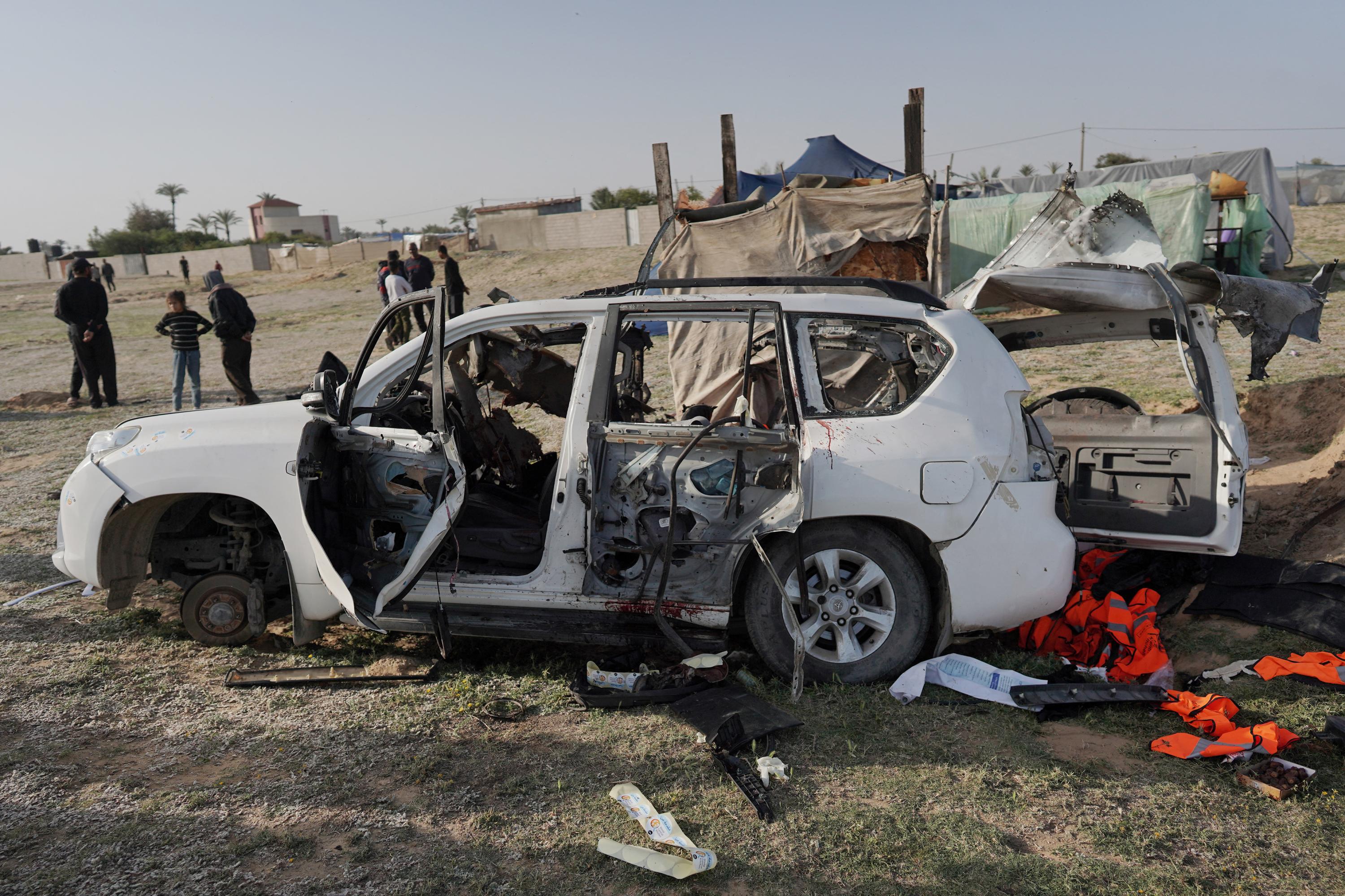 People gather around the carcass of a car used by U.S.-based aid group World Central Kitchen, that was hit by an Israeli strike the previous day in Deir al-Balah in the central Gaza Strip on April 2, 2024, amid the ongoing battles between Israel and the Palestinian militant group Hamas. The international food aid charity said on April 2 it was pausing its Gaza aid operations after seven of its staff were killed in a 