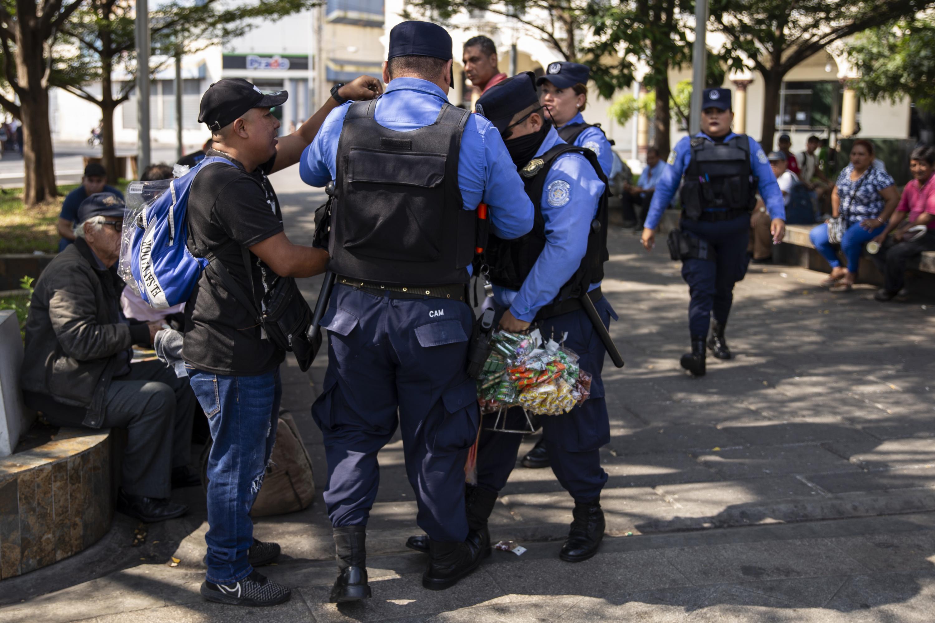 Three agents with the CAM, San Salvador’s metropolitan police department, surround Mario René Castro, a street vendor, in Plaza Libertad, in the city’s Historic Center. The agents tore up his bags and injured his left hand, strewing his candy on the ground. “These men are traitors,” said Castro, a 40-year-old native of the capital’s San Jacinto neighborhood, who has been street vending since he lost his job a year ago. On Sunday, February 14, Castro went downtown, where the city’s main blocks have become a flagship tourist destination promoted by the Bukele administration. “They [the police] came up on me by surprise and stole my $50 in sales,” he said. Castro is one of hundreds of vendors evicted from the city center. Many still attempt to sell their wares itinerantly, using carts or carrying the items and dodging CAM officers who chase them off to maintain the image of an orderly, clean, and vendor-free Historic Center. Photo by Víctor Peña.