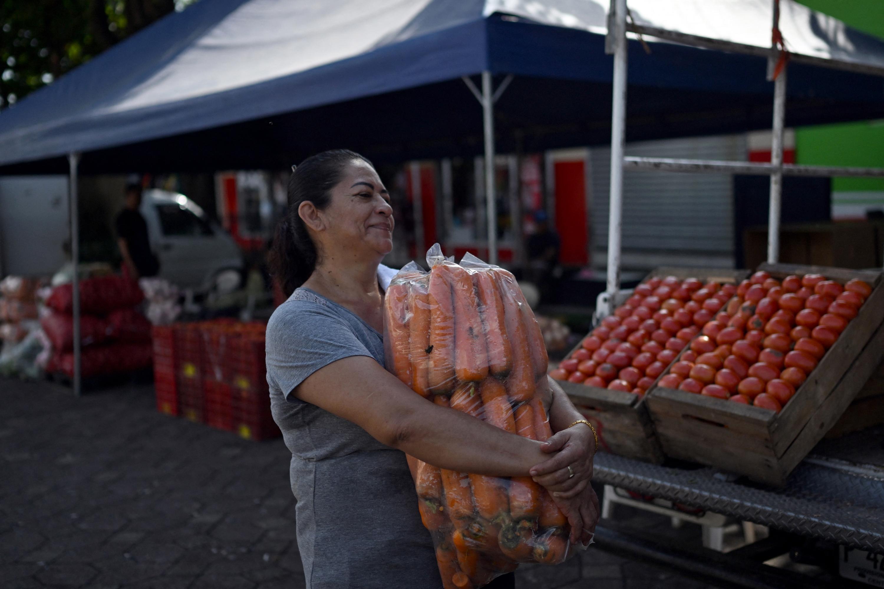 Una mujer lleva zanahorias compradas en un punto mayorista promovido por el Gobierno en el municipio de Quezaltepeque, El Salvador, el 9 de julio de 2024. Foto El Faro: AFP