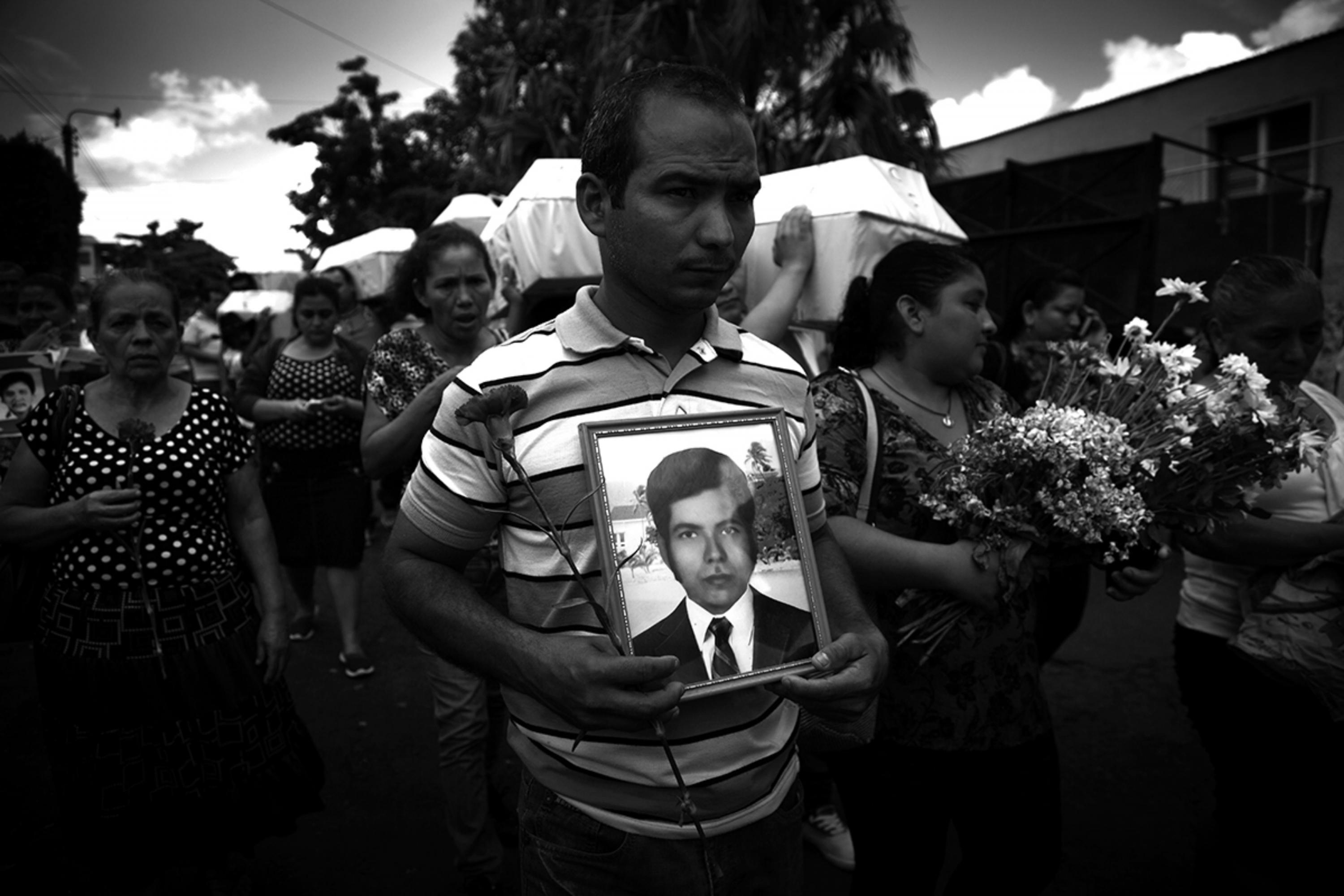 Celso Vásquez carries the portrait of his father, José Francisco Vásquez, during the burial of the victims on Aug. 26, 2016. José Francisco died in the door-to-door operation carried out by the National Guard in the hamlet of Costa Rica, Texistepeque, in 1982. State forces killed seven men in that operation. The funeral procession in homage to the victims marched for an hour and a half from the place of the wake, from the communal house of the El Palmar neighborhood of Santa Ana to the Santa Isabel General Cemetery. On the way the families chanted religious songs. The Attorney General’s Office, Human Rights Ombudsman, the coroner’s office (Medicina Legal), and the Madeleine Lagadec Center for the Promotion of Human Rights organized the funeral. Prosecutors and police were present due to the custody of the skeletons, considered as “evidence” in a case that is not being investigated. The state was supposed to cover funeral expenses, but the wake and burial were paid for by private donors.