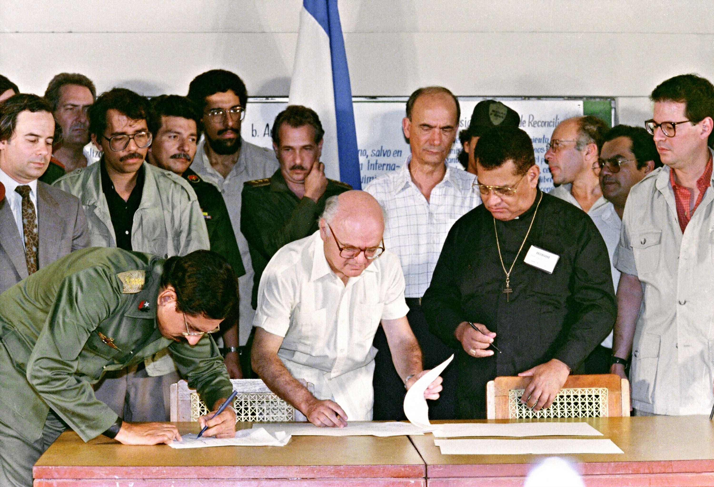 Nicaraguan Defense Minister Humberto Ortega (left) signs a cease-fire agreement with contra rebels on March 23, 1988, in Sapoa. L-to-R Nicaraguan President Daniel Ortega (with spectacles), Joao Baena Soares, general secretary of the Organization of American States, Cardinal Miguel Obando y Bravo, and Alfredo César, director of the Nicaraguan Resistance (NR). Photo Manoocher Degathi/AFP