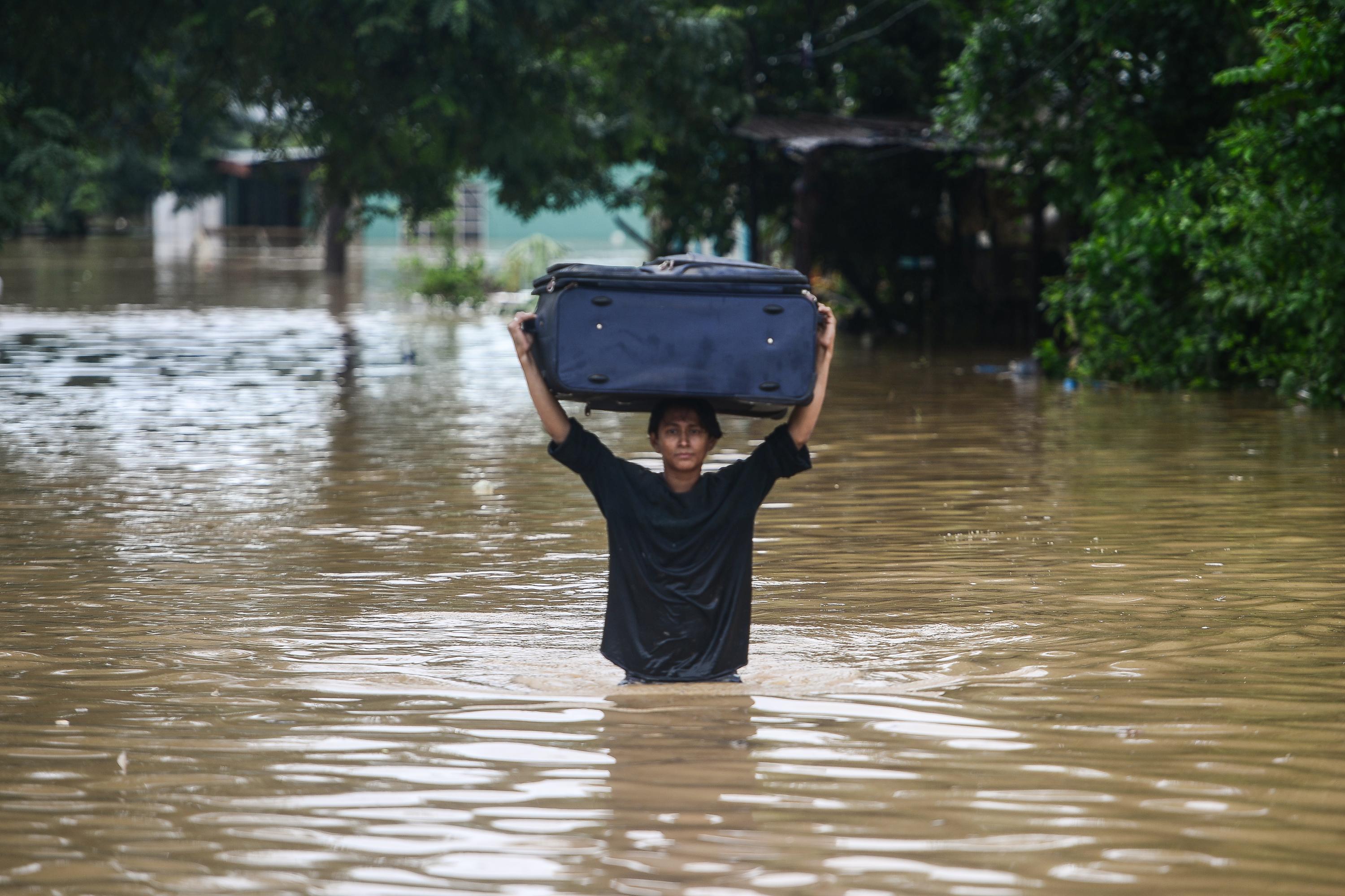 Una mujer vadea cargando un equipaje por una calle inundada tras el desborde del río Ulúa en el municipio de El Progreso, departamento de Yoro, Honduras. Foto de Orlando Sierra / AFP