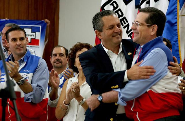 Edwin Zamora es abrazado por el presidente del Coena, Jorge Velado, después de la presentación oficial como candidato a la alcaldía por San Salvador que está en manos del partido de derecha, Arena.  El vicepresidente de ideología, Ernesto Muyshondt (a la izquierda) fue blanco de insultos por parte de Zamora en un audio que se coló al público hace un año. Foto El Faro/Fred Ramos