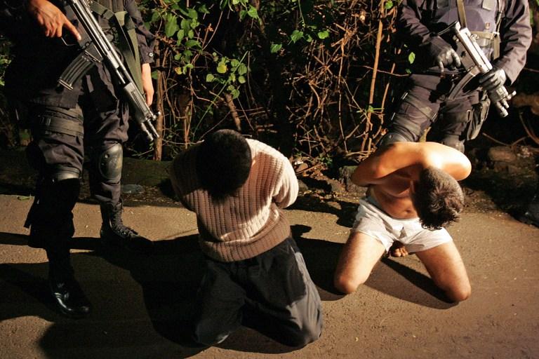 Imagen de archivo que muestra a dos agentes del Grupo de Reacción Policial (GRP), la unidad élite de la Policía Nacional Civil (PNC), que custodian a dos pandilleros de la Mara Salvatrucha, tras un operativo nocturno en el municipio de La Libertad. Foto Yuri Cortez (AFP).