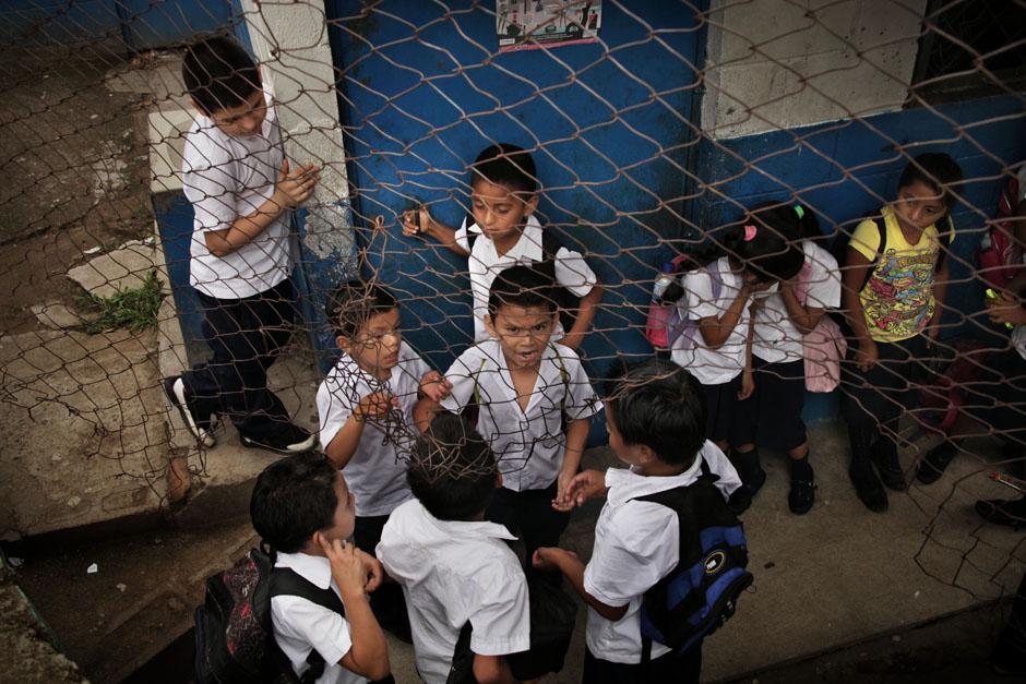 Niños de segundo grado esperan el inicio de clases reunidos alrededor de un líder de su aula. La malla deteriorada debería proteger las instalaciones del ingreso de extraños. Panchimalco fue el centro de las noticias nacionales cuando en 2012 fueron asesinadas más de 80 personas, pues el año anterior, 2011, habían ocurrido 46 homicidios en este municipio. El acoso de los pandilleros a algunos centros escolares del municipio llegó a ser parte de la cotidianidad de alumnos y maestros.