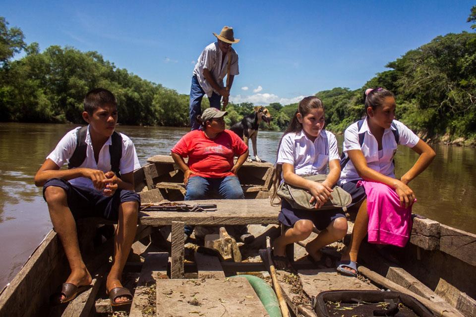 Nelson, Darling y Tatiana recorren un tramo del río Lempa para llegar a la escuela Cantón San Antonio Grande. Los acompaña el padre de una de ellas. La persona que antes los transportaba para atravesar el río dejó de hacerlo debido a que fue amenazada por las pandillas del cantón San Antonio Grande. El uso de la lancha es de 25 centavos de dólar por viaje.