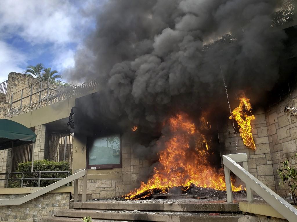 El 31 de mayo de 2019, la entrada de la Embajada de Estados Unidos en Tegucigalpa arde en llamas tras una demostración de un grupo de manifestantes que salieron a las calles a protestar en contra de la privatización de los servicios de educación y salud. El gobierno impulsó un decreto. Miles de profesores, doctores y estudiantes se sumaron a las protestas en contra de las medidas impulsadas por el presidente Juan Orlando Hernández.Foto, Orlando Sierra, AFP.