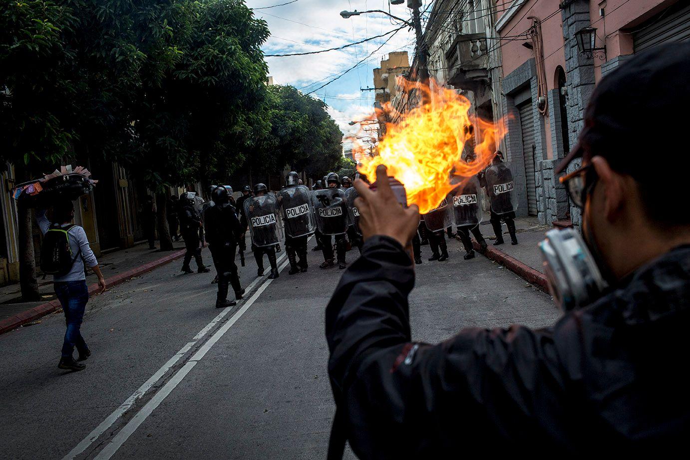 A protester burns gas in front of a riot squad. /