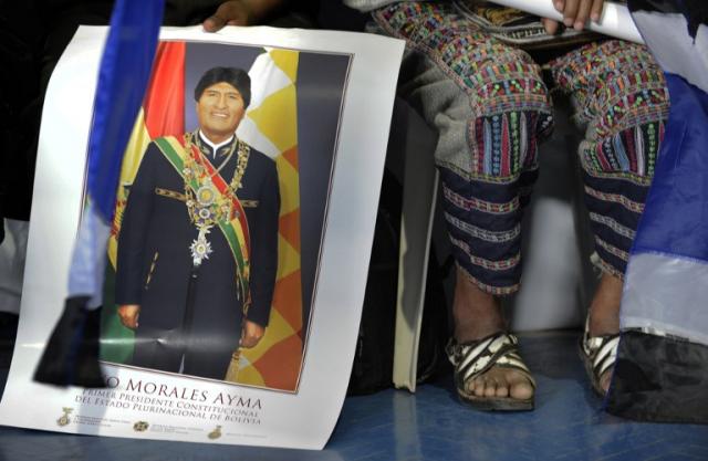 Un hombre sentado junto a una mujer indígena sostiene un póster de Evo Morales en la ciudad de Cochabamba, donde el presidente boliviano fue homenajeado. tras su accidentado viaje a Europa. Foto Jorge Bernal (AFP).﻿" /></div> <figcaption class=