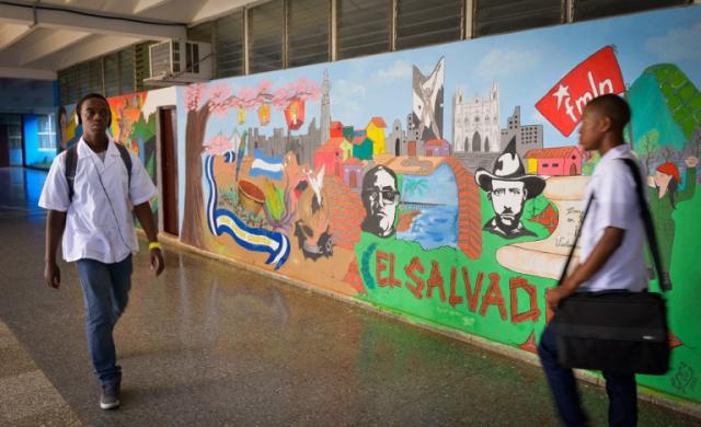 Dos estudiantes de la ELAM caminan frente a un mural dedicado a El Salvador pintado en uno de los muros, en el que hay referencias expresas al FMLN. Foto Adalberto Roque (AFP)﻿.