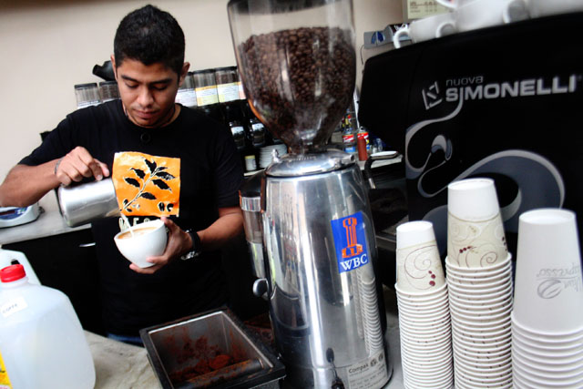 Alejandro, junto al molino de café y junto a la máquina de espresso, preparando un capuchino.