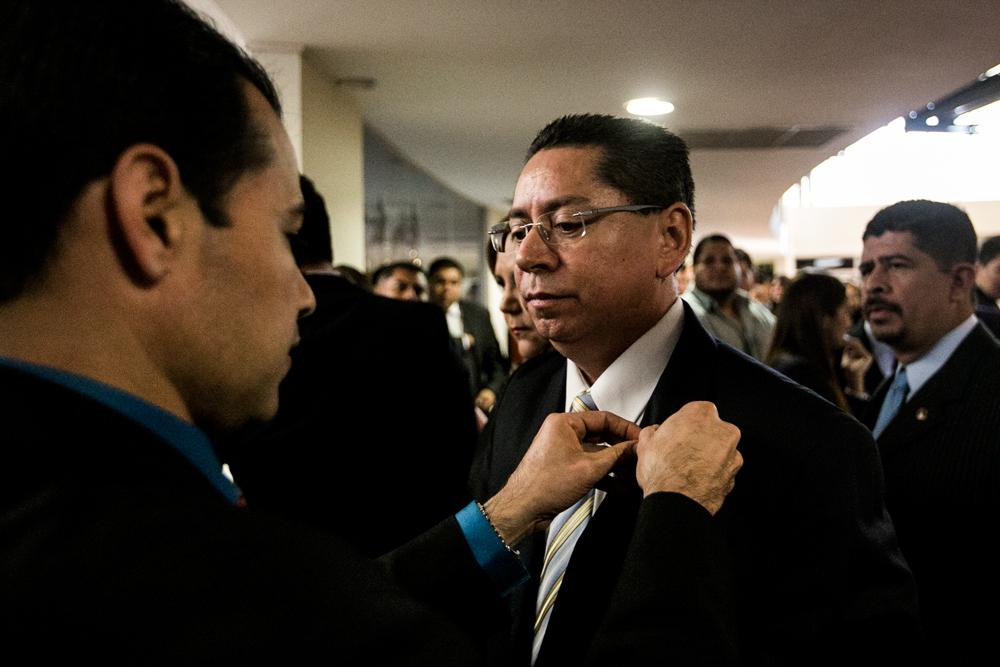 Érick Álvarez, uno de los acompañantes del recién electo fiscal general Douglas Arquímides Meléndez Ruiz, le pone un pin oficial de la FGR en su traje. Foto: Fred Ramos