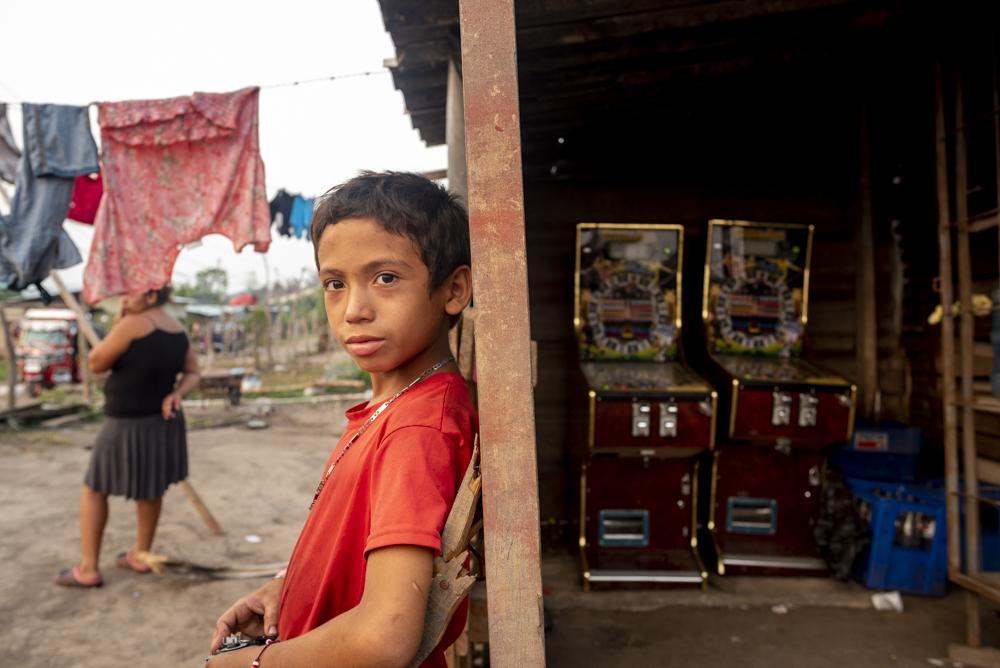 A young boy stands outside of a bodega with gambling machines inside.