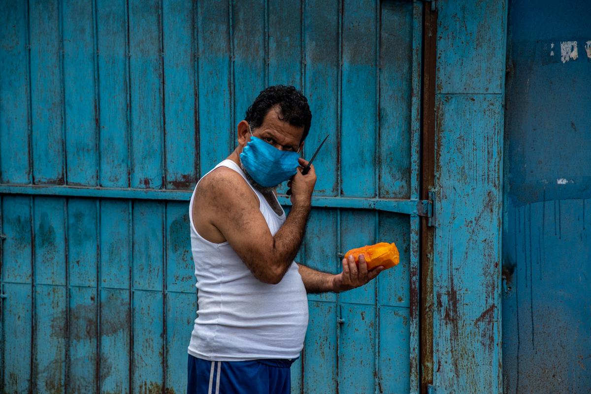 A man wearing a protective mask cuts a papaya in the central marketplace of San Pedro Sula. May, 23rd 2020. Photo: Seth Berry