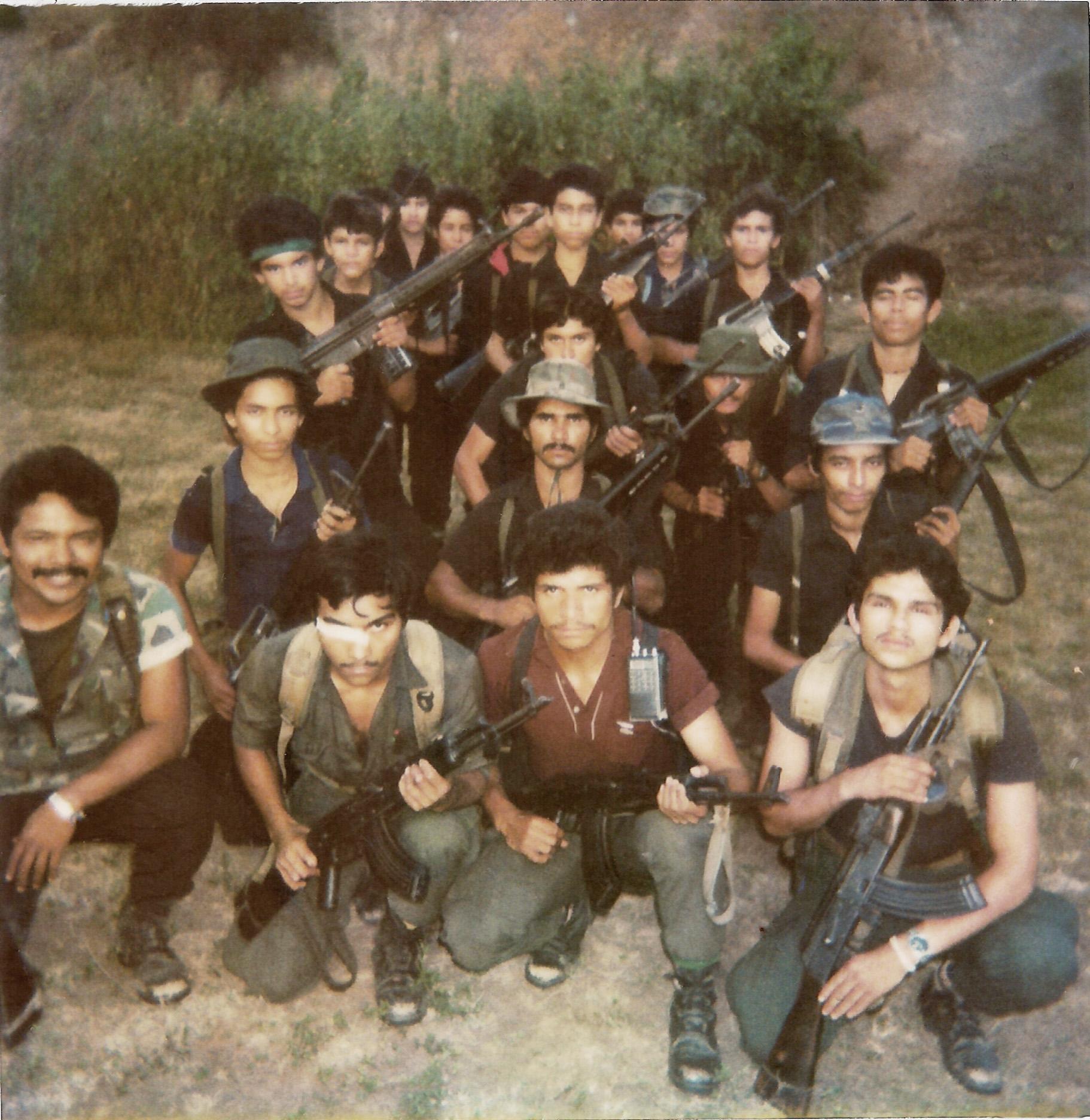 Fotografía de una unidad de las Fuerzas Populares de Liberación (FPL) tomada en San José Las Flores, Chalatenango, en el mes de octubre de 1989. Este pelotón se montó en preparación de la ofensiva de 1989. De las 20 personas en la foto, 18 sobrevivieron la guerra. En la posguerra algunos se asentaron en las repoblaciones, otros emigraron al Norte, algunos se convirtieron en PNC, y uno logró estudiar medicina en Cuba. A lo largo del tiempo, varios excombatientes de esta foto obtuvieron empleo mediante sus conexiones con el FMLN.