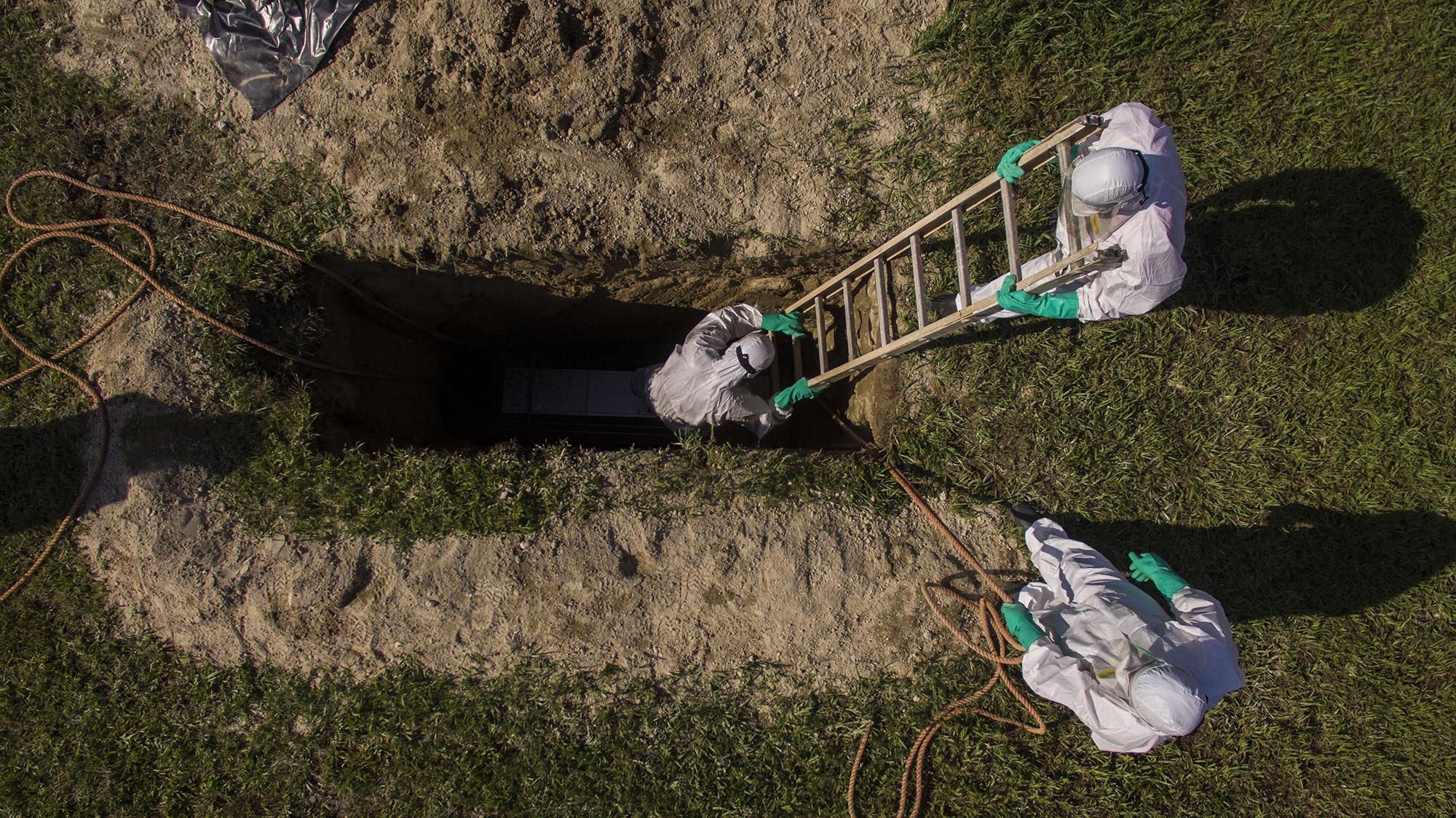Empleados municipales de Soyapango acomodan un féretro en una fosa, durante un entierro realizado con el protocolo para víctimas de covid-19, en la tarde del 11 de junio. Foto de El Faro: Víctor Peña. 