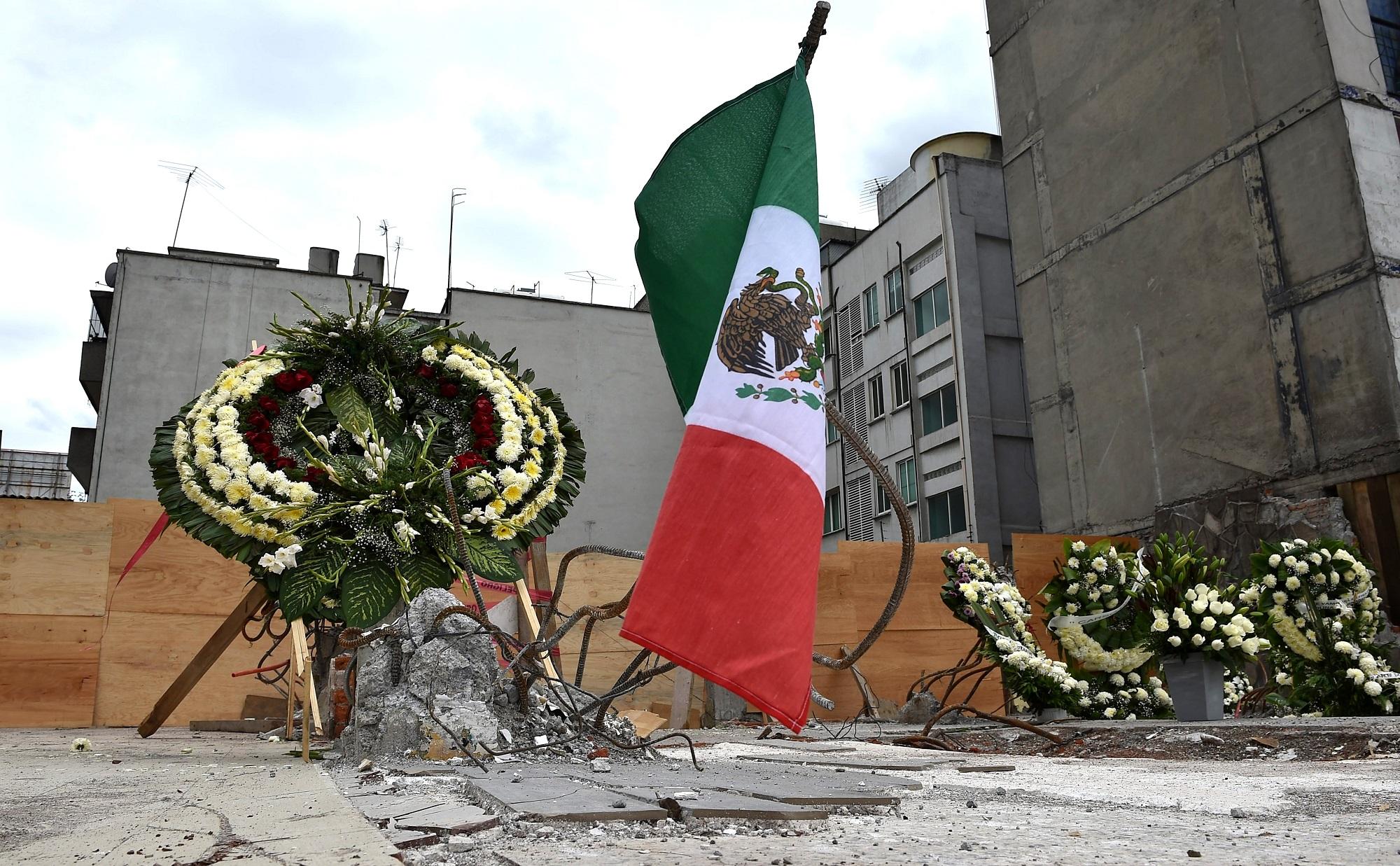 Una bandera de México y una corona de flores para homenajear, en el lugar en el que colapsó un edificio, a los fallecidos en el terremoto del 19 de septiembre de 2017. Foto Yuri Cortez (AFP).