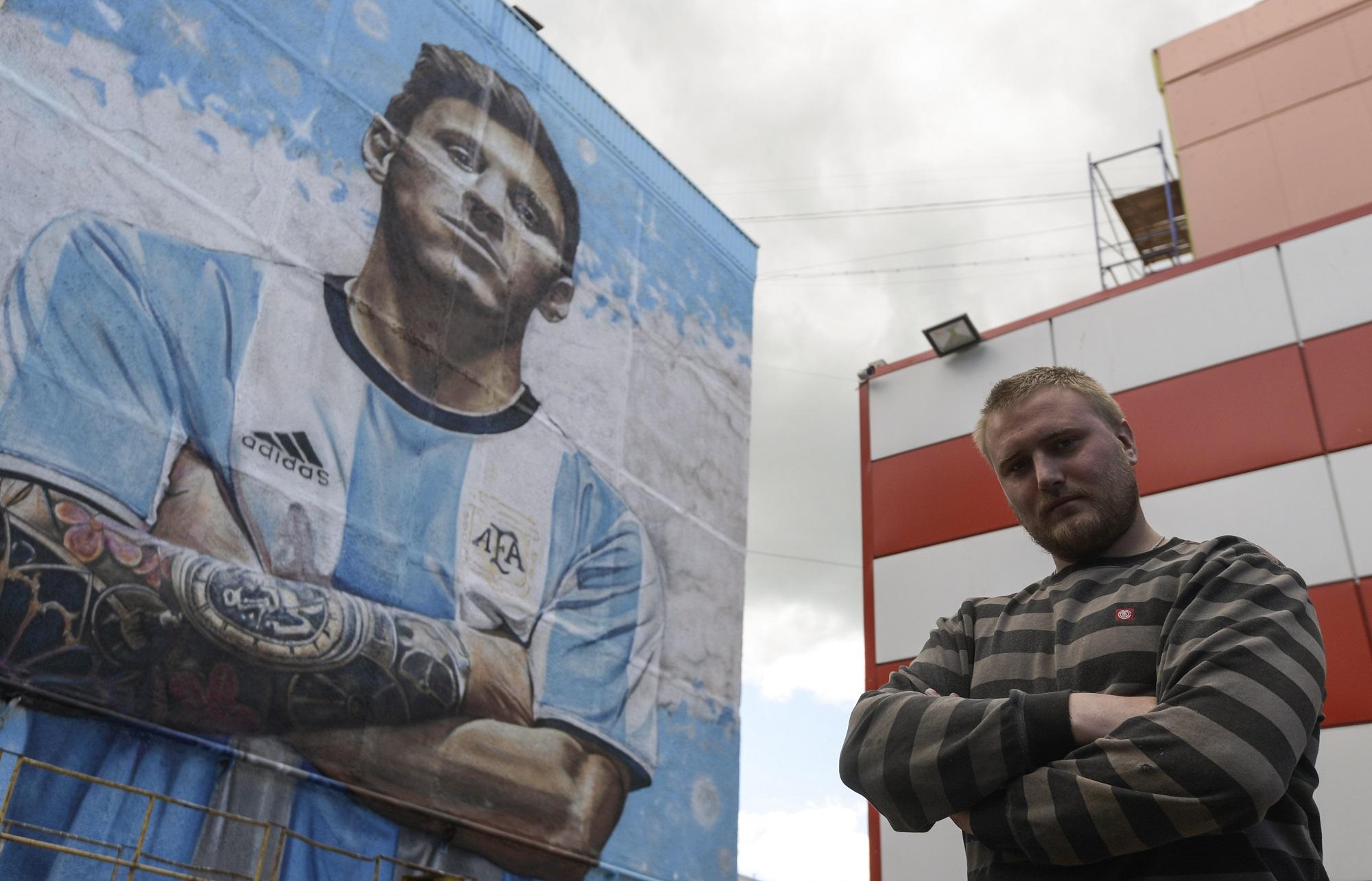 El artista Sergey Erofeev posa frente al gigantesco grafiti de Lionel Messi que ha pintado en la calle principal de Bronnitsy, la pequeña ciudad rusa que la selección argentina ha hecho su base en los días previos al Mundial. Foto Juan Mabromata (AFP).