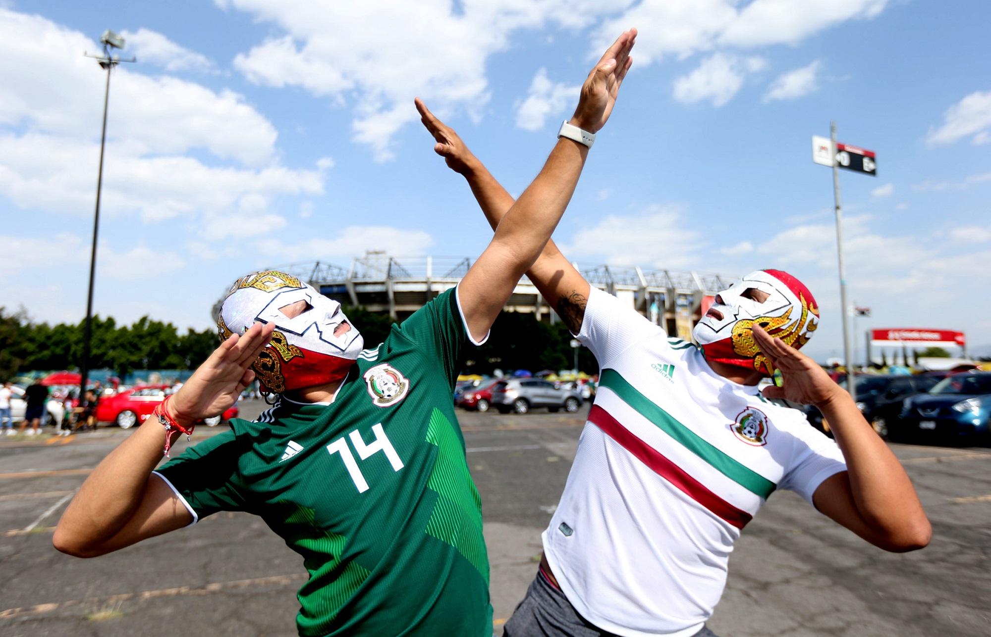 Dos aficionados de la sección azteca posan con el gesto con el que Cuauhtémoc Blanco celebraba los goles para el fotógrafo de la agencia Xinhua frente al mítico Estadio Azteca de Ciudad de México. Foto Xinhua.
