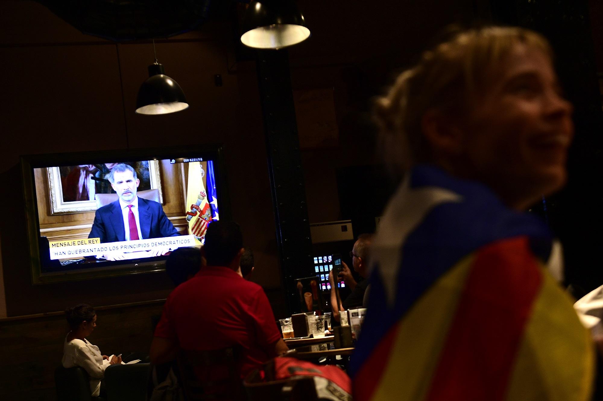 Una mujer con la versión independentista de la bandera de Cataluña sonríe en un bar de Barcelona mientras por televisión transmitían el discurso del rey Felipe VI, el jefe de Estado español, quien la noche del 3 de octubre habló por primera vez desde el referéndum del domingo sobre el conflicto. Foto Pierre-Philippe Marcou (AFP).