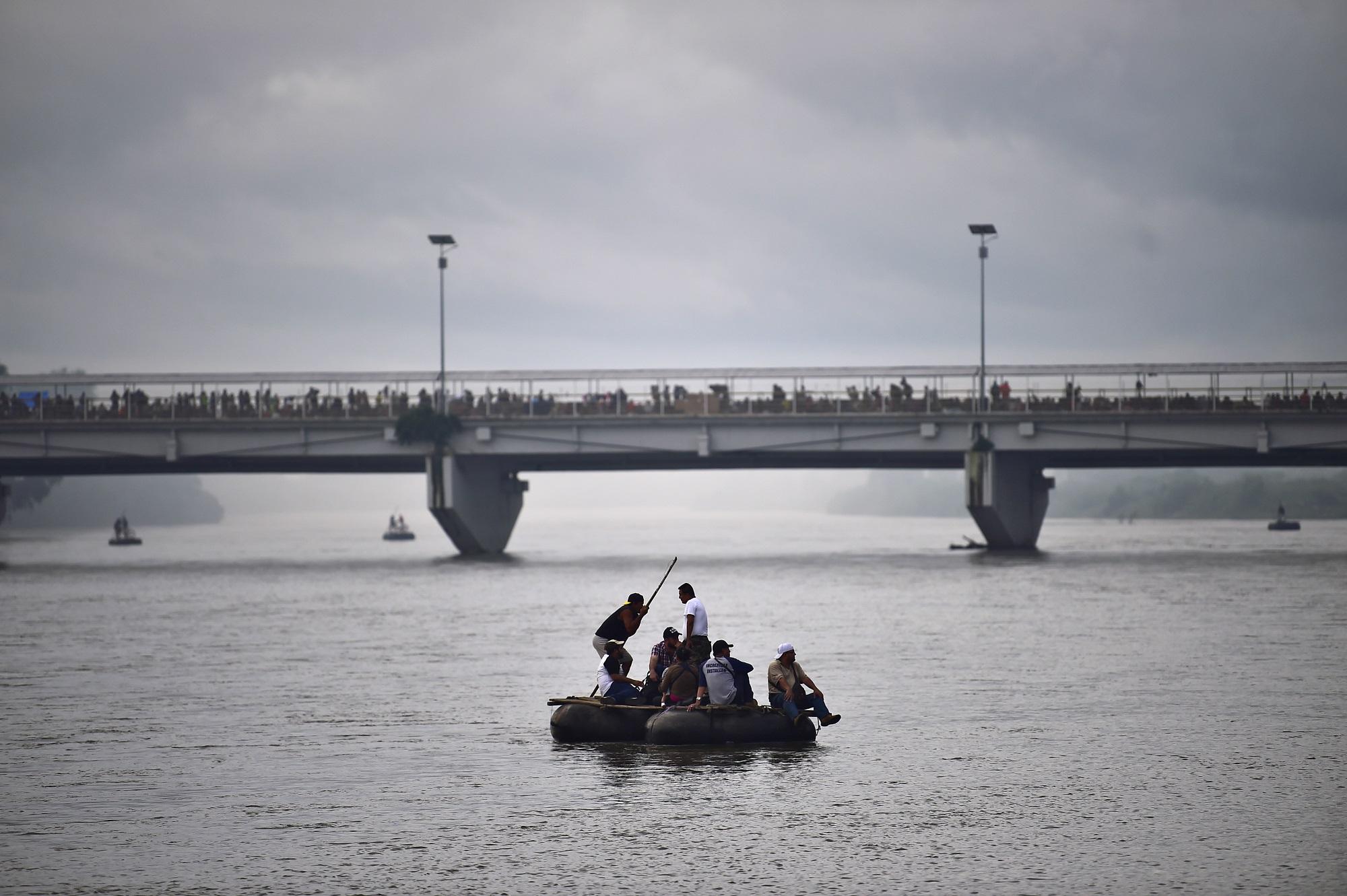 Un pequeño grupo de migrantes centroamericanos cruza en una balsa hechiza el río Suchiate, la frontera entre Guatemala y México. Al fondo, centenares se agolpan en el puente, cerrado por las autoridades mexicanas. Foto Pedro Pardo (AFP).