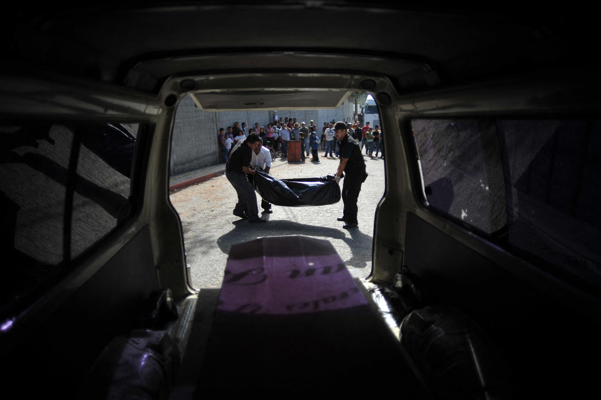 Personal forense y empleados de una funeraria cargan en un vehículo los cuerpos con signos de tortura de dos hombres asesinados que fueron encontrados en una calle del municipio Palin, departamento de Escuintla, 35 km al sur de la Ciudad de Guatemala, el 21 de noviembre de 2011. Foto de El Faro: Johan Ordóñez/AFP.