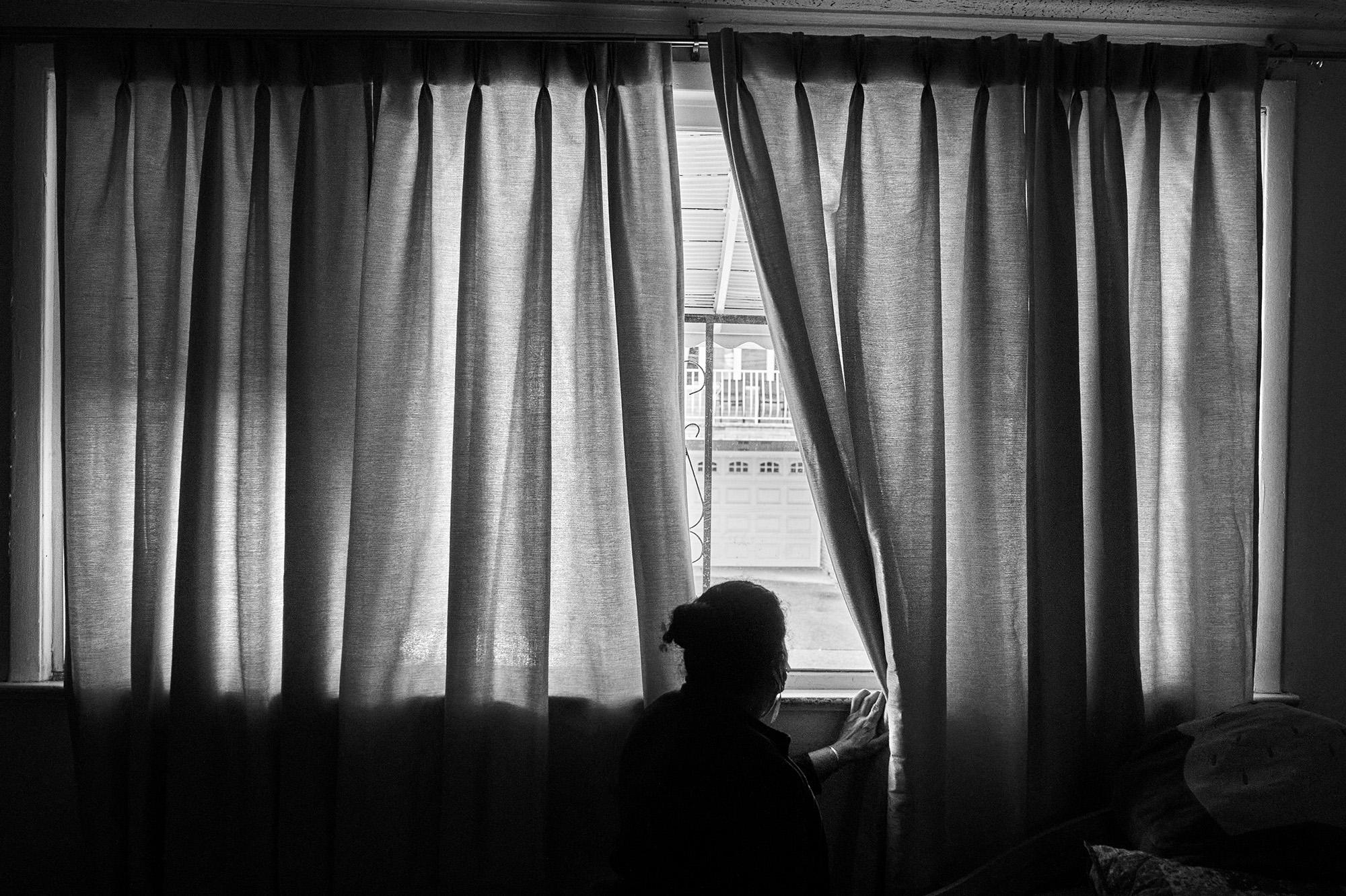 Nidia Portillo looks out the window of the room she shares with her autistic daughter in New Jersey. Born in El Salvador, Nidia moved to the United States in 1994 and raised her children here with her husband Aquilino. During the Covid-19 pandemic, 13 people lived in her home. They all got sick. Photo: Edu Ponces/Ruido Photo
