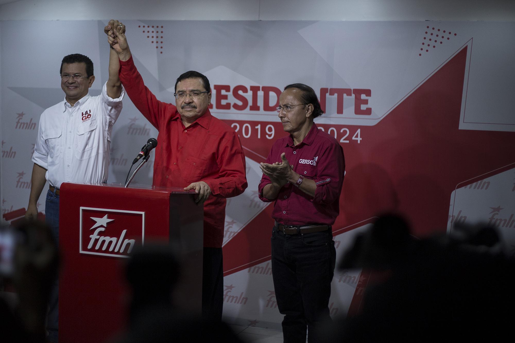 El secretario general del FMLN, Medardo González, levanta la mano al ganador, Hugo Martínez, ganó por ventaja de más de 12 mil votos a Gerson Martínez.  Foto de El Faro, por Víctor Peña.