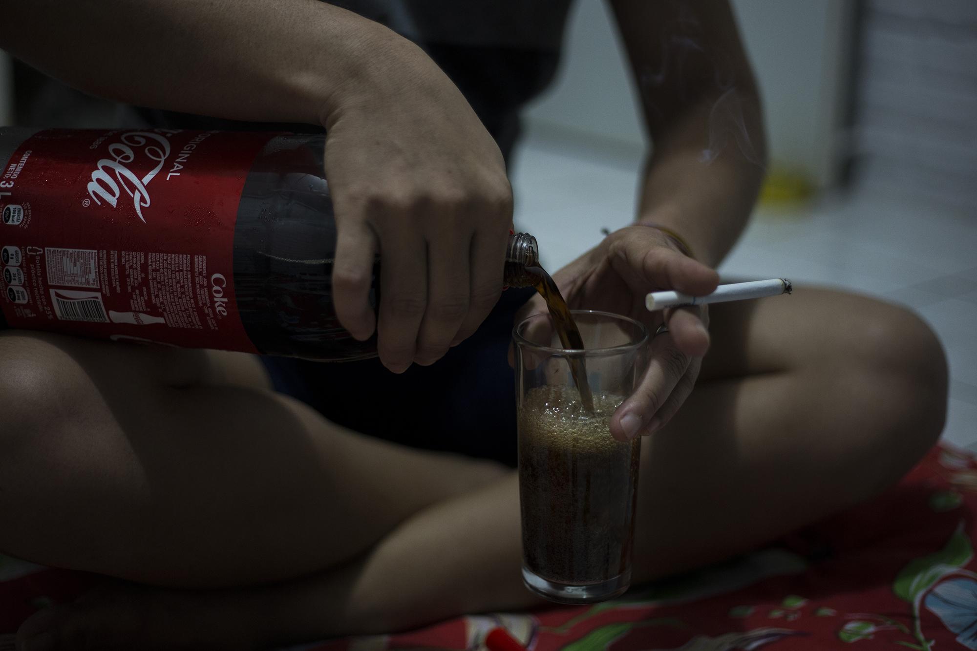 Doctor Veneno, uno de los refugiados en la casa de seguridad, conversa con un cigarrillo entre los dedos y se sirve Coca Cola, pasar el tiempo. El encierro ha acostumbrado a los estudiantes a largas jornadas de conversación nocturna. Foto: Víctor Peña.