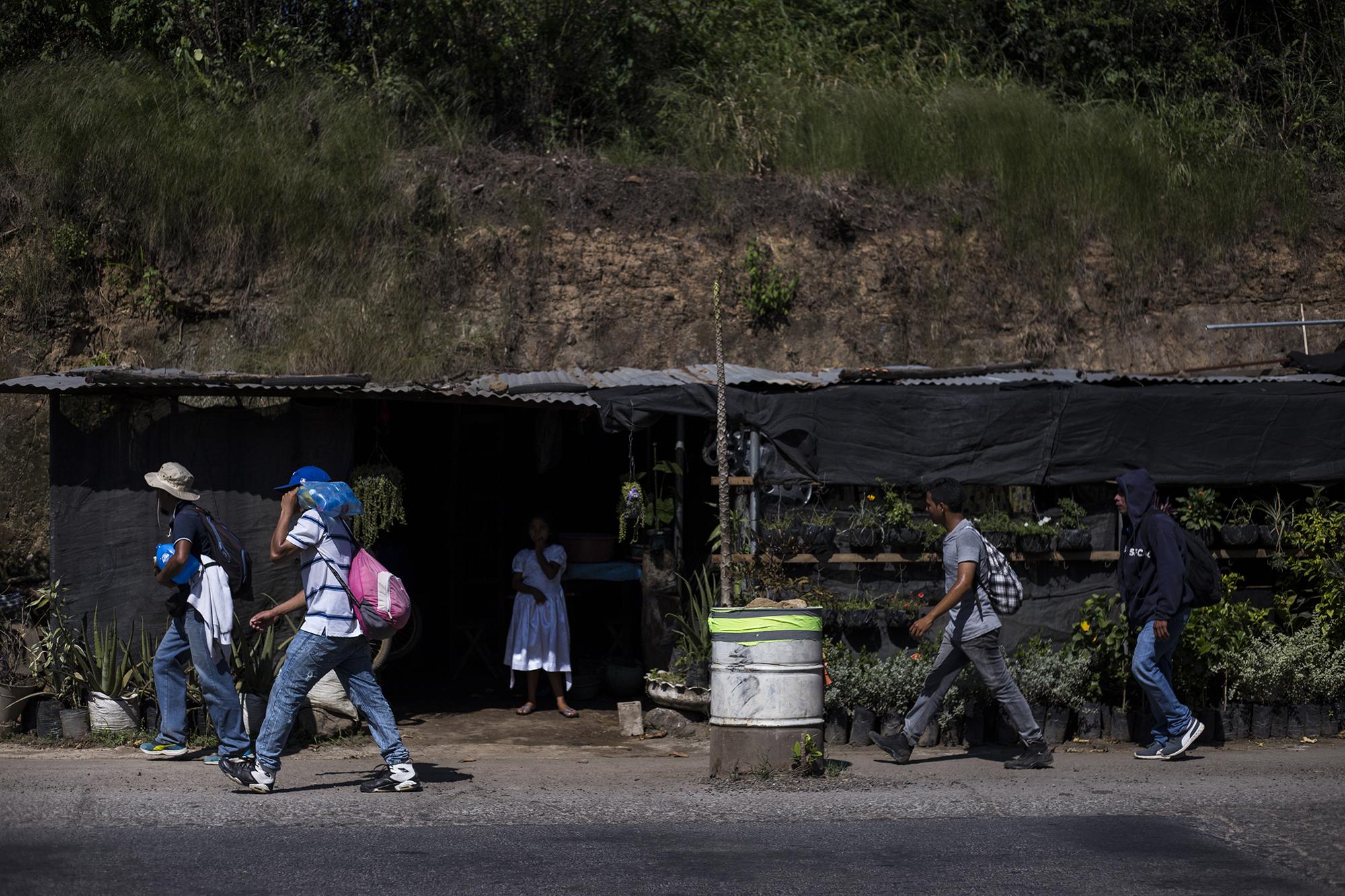 Migrantes pasan frente a una vivienda a la orilla de la carretera, en el cantón Metalío, del municipio de Acajutla, en Sonsonate. Estos eran parte de un grupo que perdió el paso de la caravana. Foto: Víctor Peña.