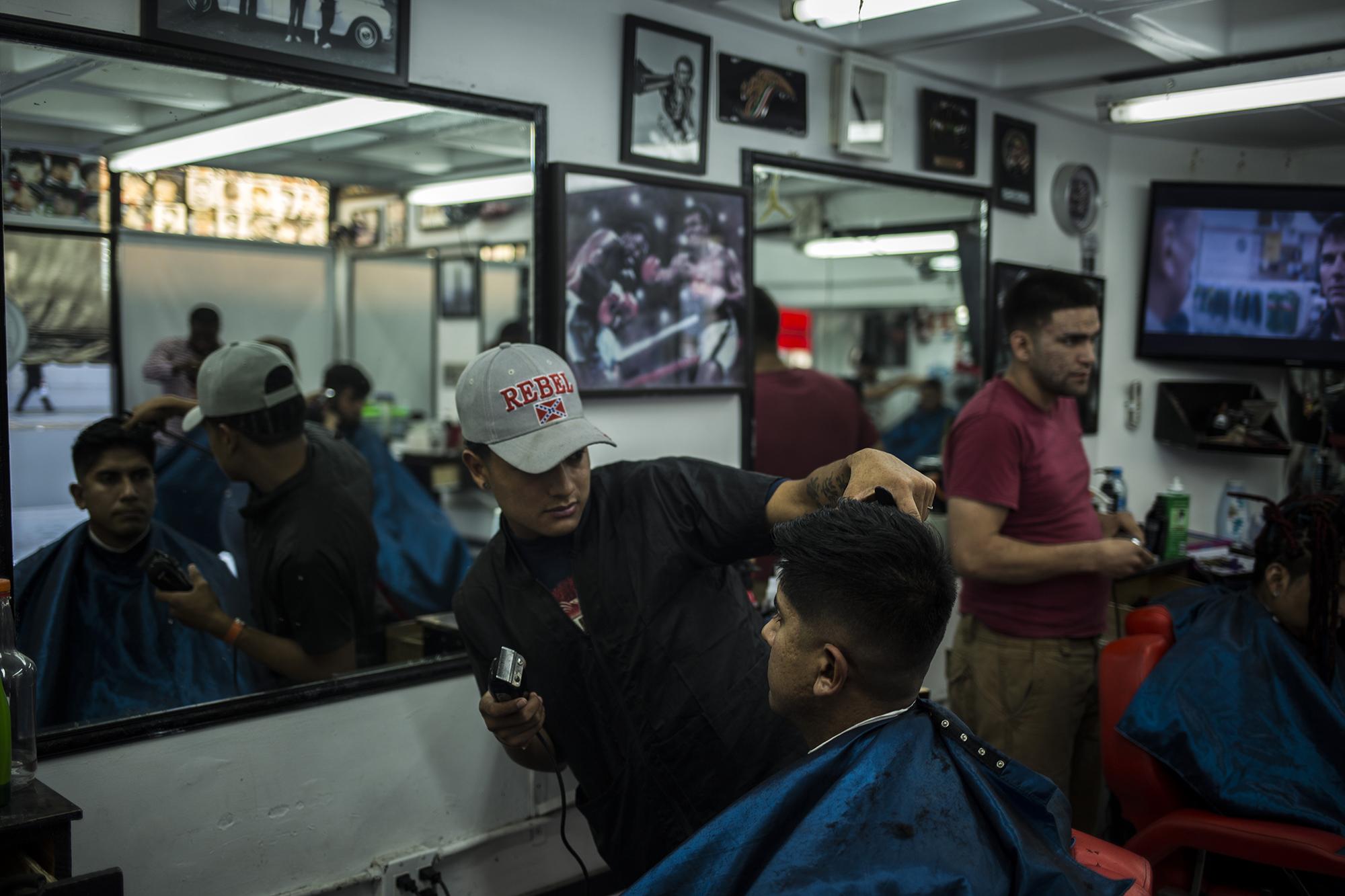 Gerson Javier Acosta ya trabaja permanentemente en una peluquería en el corazón de la zona viva de Tijuana. A sus 21 años. se ganó la vida como peluquero en el trayecto de la caravana de migrantes centroamericanos por todo México. Es una peluquería moderna, donde realiza diez cortes de cabello por día. 