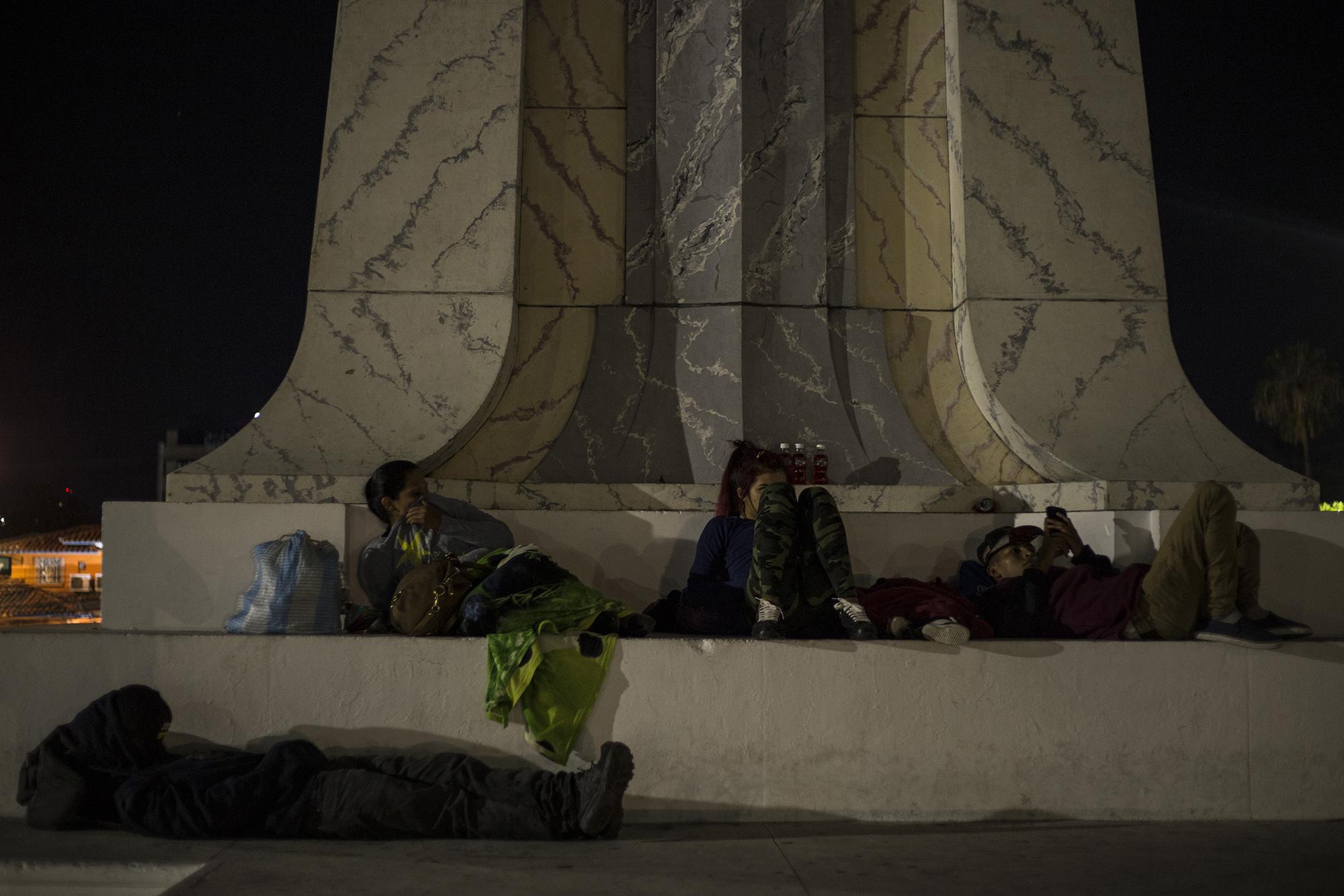 Junto a otros migrantes, Kevin (de gorra) y su pareja esperan que amanezca en la base del monumento al Divino Salvador del Mundo. Foto: Víctor Peña.