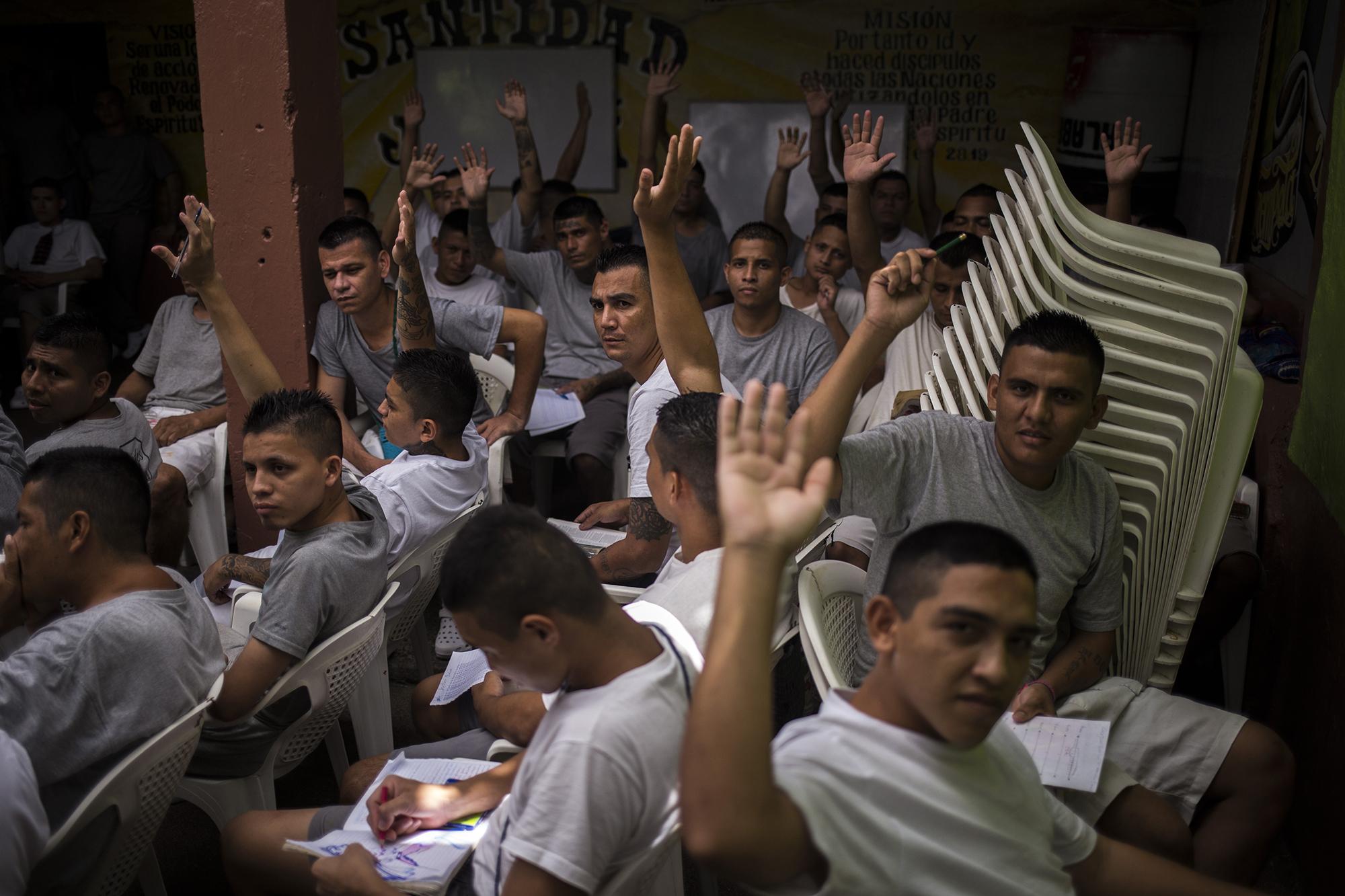 Exmiembros de la MS-13 levantan la mano para identificarse ante la pregunta del fotoperiodista. Unos 150 ex emeeses conviven con más de 1 000 ex dieciocheros en el penal de Gotera. Foto de El Faro: Víctor Peña. 