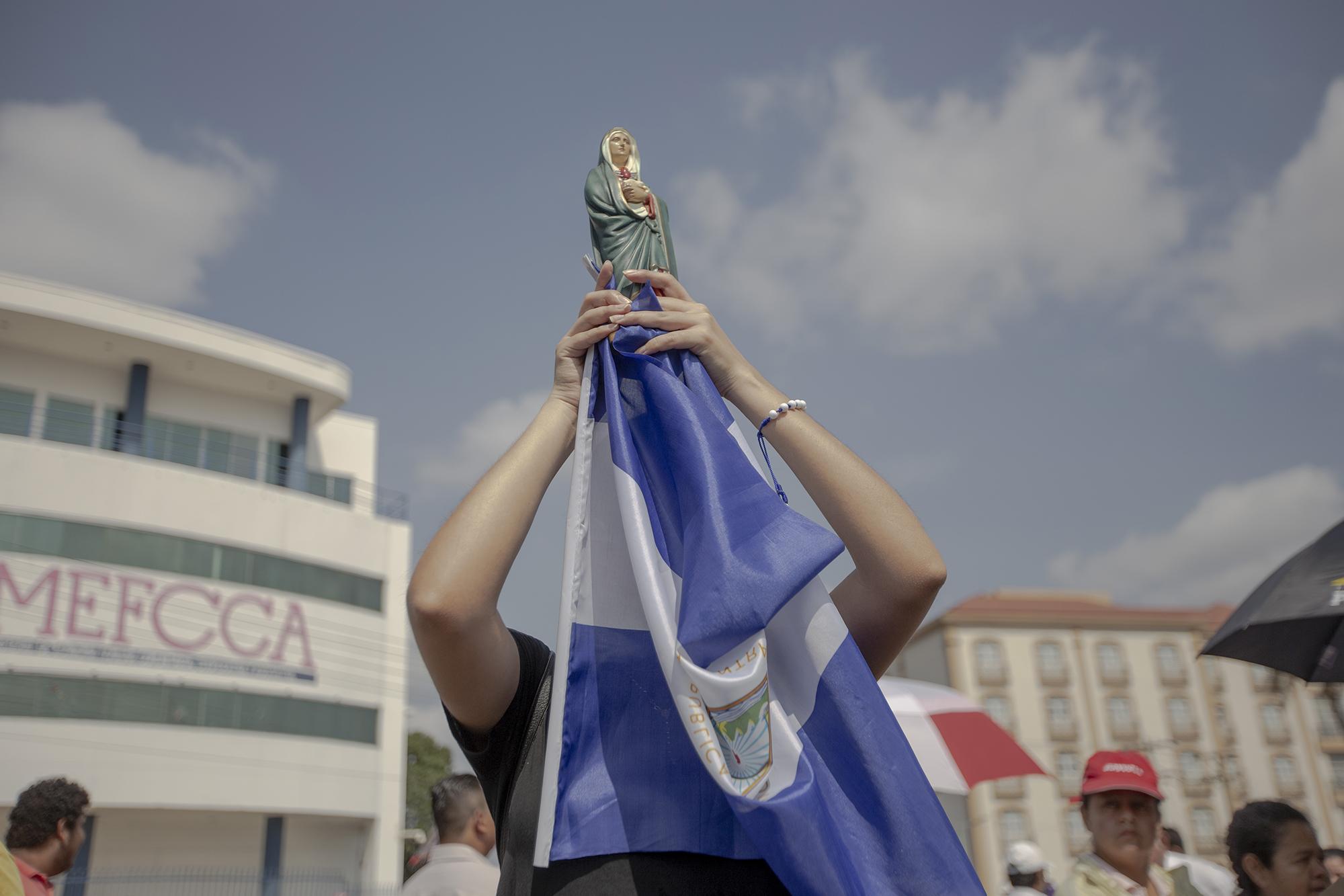 Una mujer nicaragüense carga una imagen de la Virgen Dolorosa con una bandera de Nicaragua durante la procesión del viernes santo en las cercanías de la catedral de Managua. La mujer, que no brindó su nombre por miedo a represalias de parte del gobierno o de paramilitares, asegura que llevar la bandera a la procesión es un acto de protesta y de fe por el sufrimiento que ha tenido el país desde abril de 2018, cuando se desató una crisis política seguida de una brutal represión y persecución por parte del Estado y grupos orteguistas contra los opositores políticos. En el último capítulo de la crisis, el régimen excarceló el 30 de diciembre a 91 presos políticos. Foto: Fred Ramos