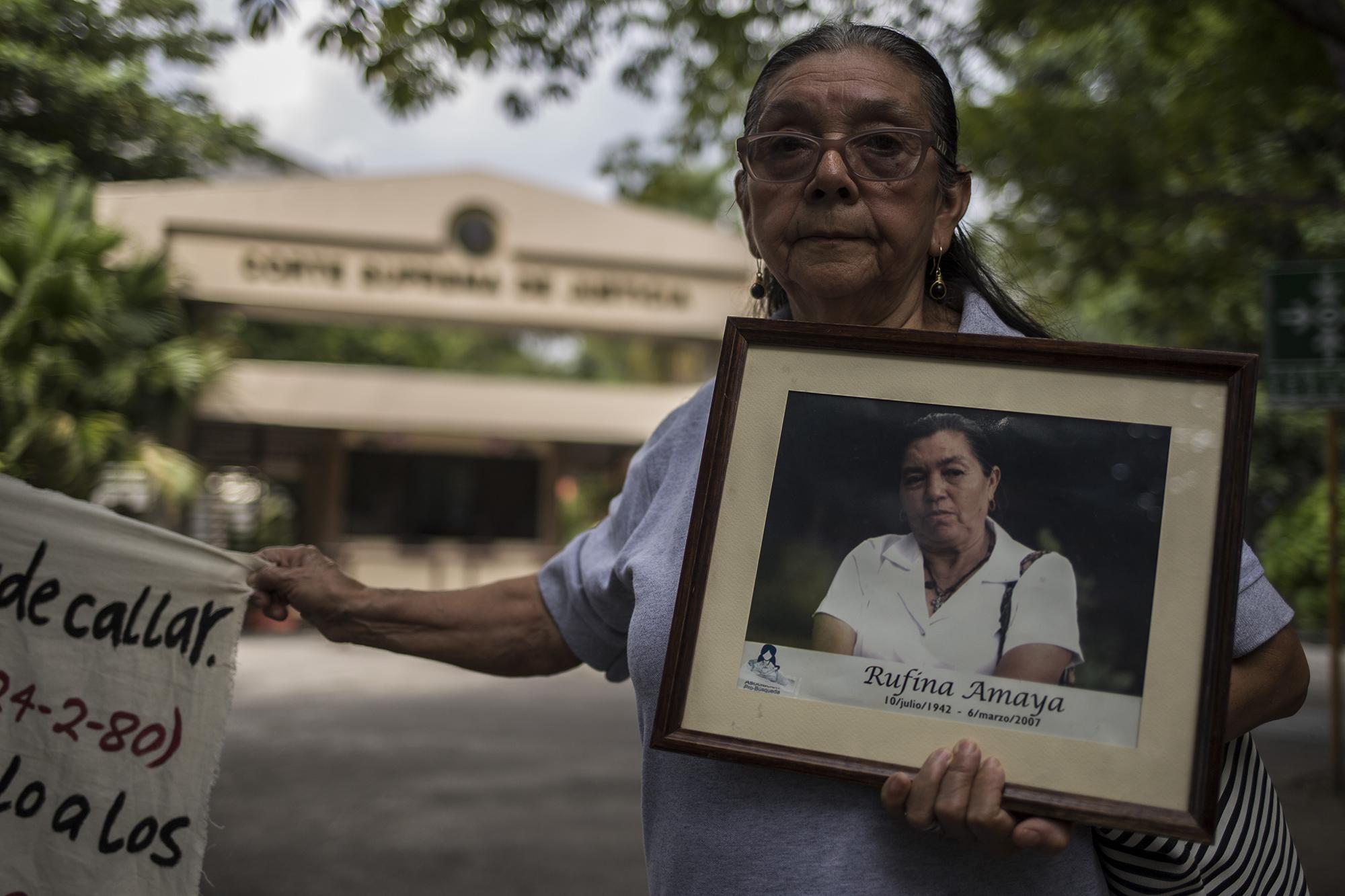 María Inés Durán, de 74 años, llegó a la Asamblea para exigir justicia por su hijo desaparecido hace 30 años. En el cuadro carga la imagen de Rufina Amaya, la sobreviviente de El Mozote que denunció una masacre en ese caserío y otros sitios aledaños perpetrada por el Ejército en 1981. Foto: Víctor Peña.