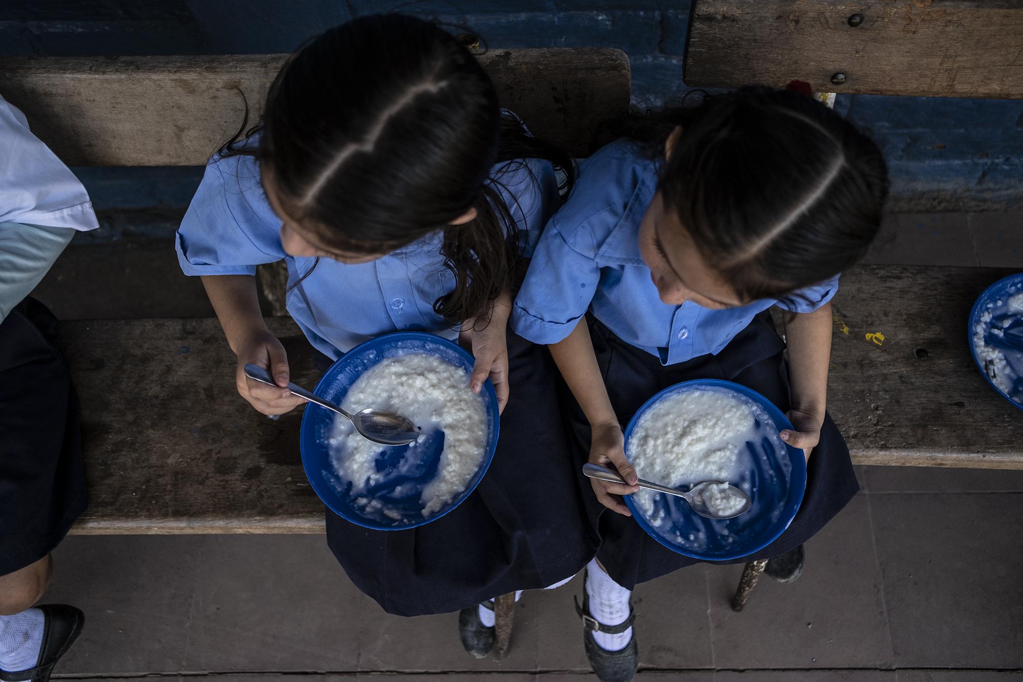 Dos niñas reciben su merienda en el Centro Escolar Caserío El Tule, una de las escuelas excluidas de la entrega de leche fluida del Programa Vaso de Leche de El Salvador. A cambio, les entregan leche en polvo de otro programa de gobierno.  En febrero de 2019, la empresa estatal ANDA le cortó el servicio de agua a la escuela. Foto, Carlos Barrera.