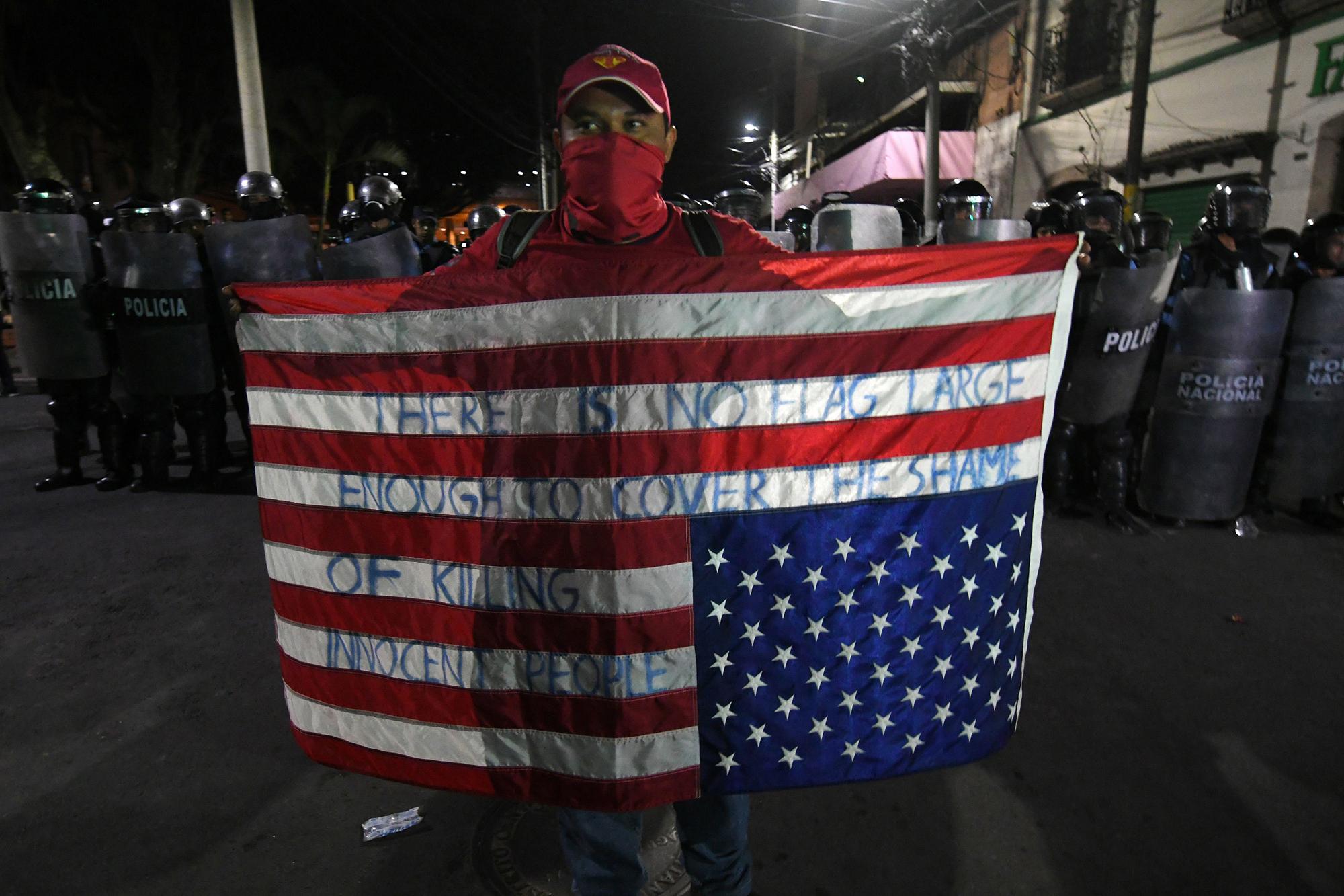 An opposition supporter holds a US flag upside down in front of a line of riot police during a protest demanding the resignation of Honduran President Juan Orlando Hernandez for his alleged links to drug trafficking in the surroundings of the Congress building in Tegucigalpa on October 9, 2019. - Opposition legislators tried to start an impeachment to President Hernandez Tuesday night at the Congress accusing him of drug trafficking, a measure with few possibilities of success in a parliament with a majority of pro-government legislators. A US prosecutor had said on October 2 at the opening of the trial of the Honduran president