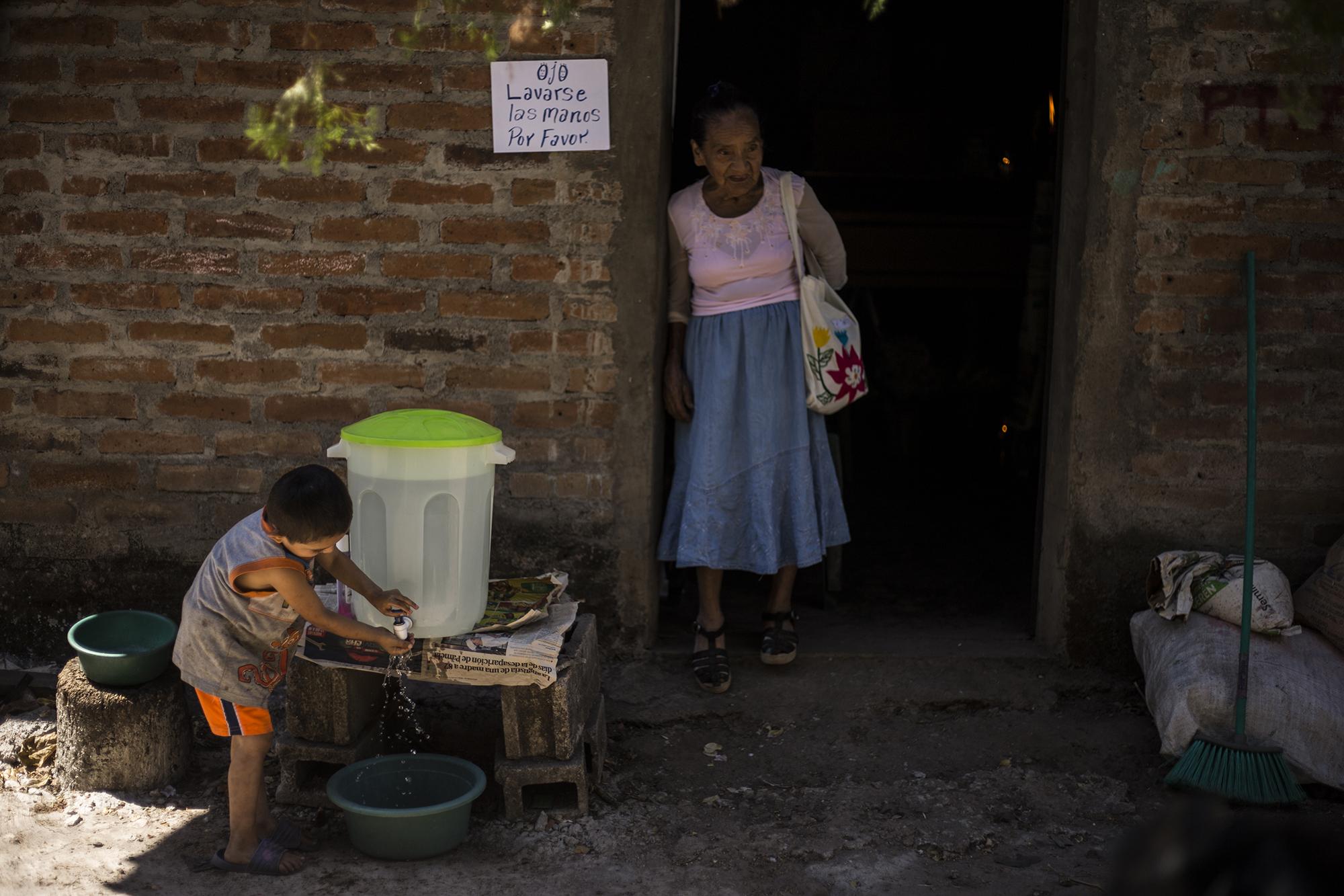 Two-year-old Auner Amaya washes his hands. In the doorway, Don Ángel’s 87-year-old sister, María Santos. When news spread of Ángel